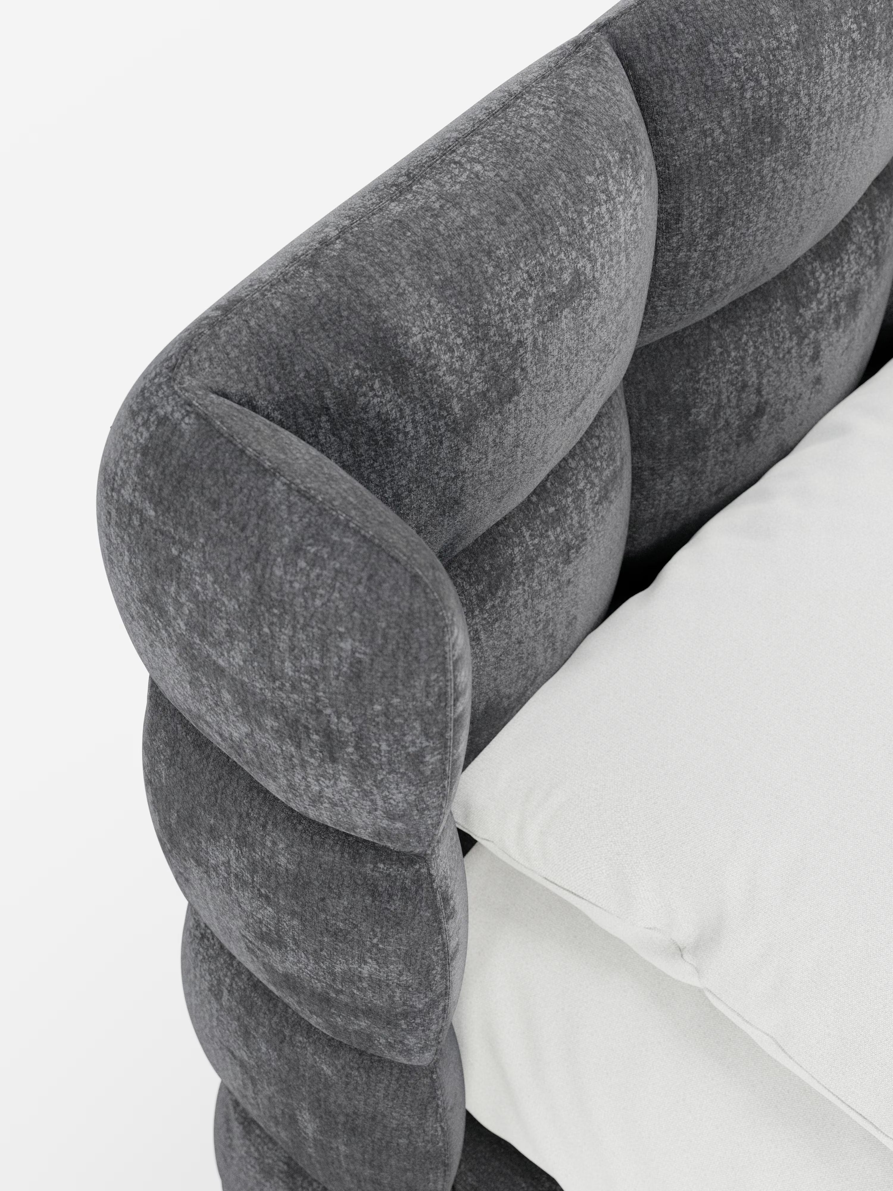 Primo piano del letto imbottito RAGNAR con contenitore e testiera capitonné avvolgente di Letti.store, caratterizzato da un elegante e soffice tessuto grigio scuro certificato Oeko-Tex®. La testiera arrotondata e trapuntata presenta un classico design capitonné, impreziosita da un cuscino di seduta bianco a contrasto. I materiali morbidi e le linee moderne creano un look accogliente ma allo stesso tempo elegante sullo sfondo bianco a tinta unita.