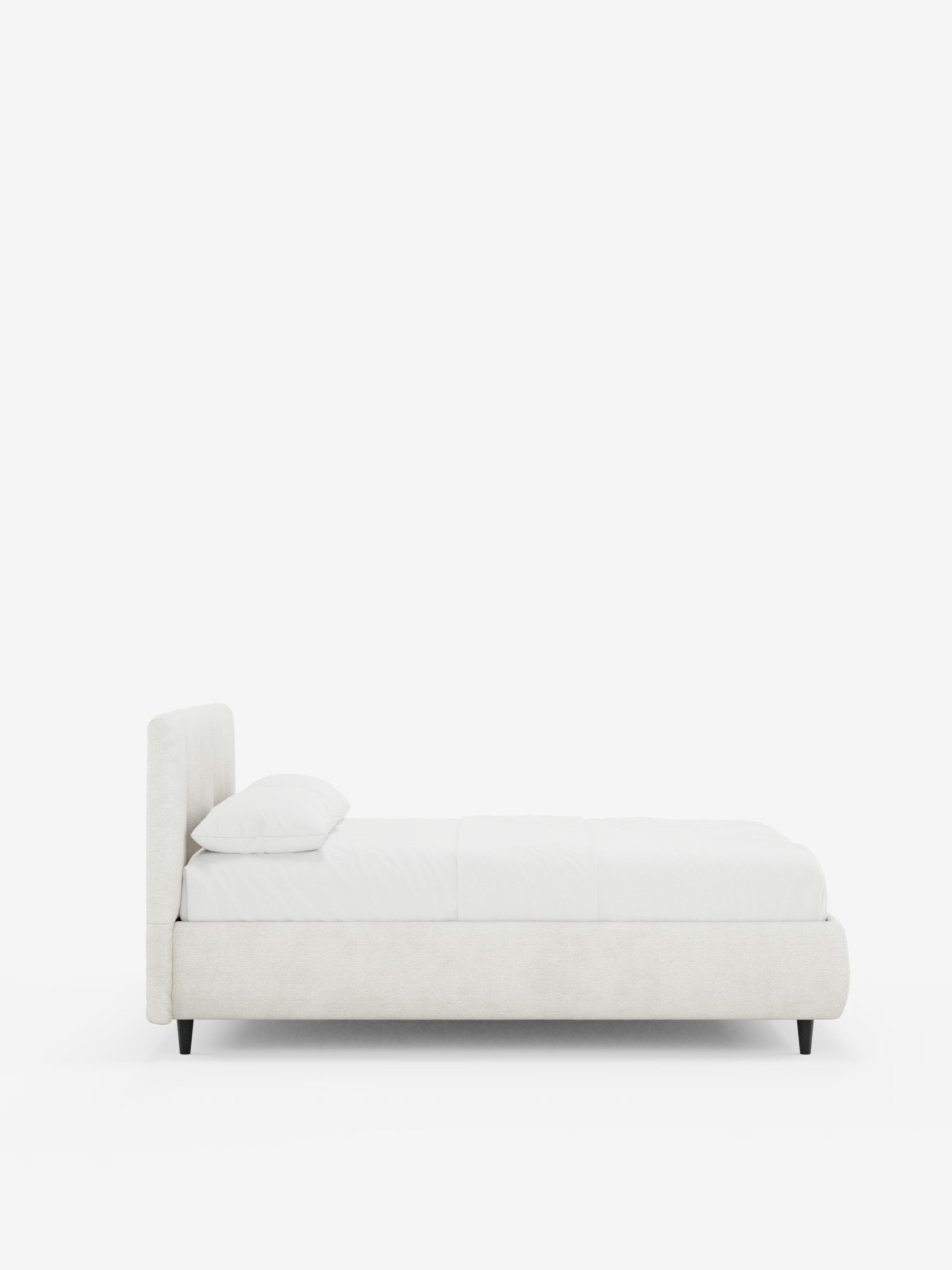 Vista laterale del letto imbottito ARKAM con vano contenitore e testiera a cuciture verticali di Letti.Il prodotto, caratterizzato da un design minimalista in stile shabby chic in tessuto bianco certificato Oeko-Tex®, presenta una testiera imbottita con cuciture verticali, biancheria da letto bianca con un unico cuscino e gambe corte nere, il tutto su uno sfondo bianco a tinta unita.