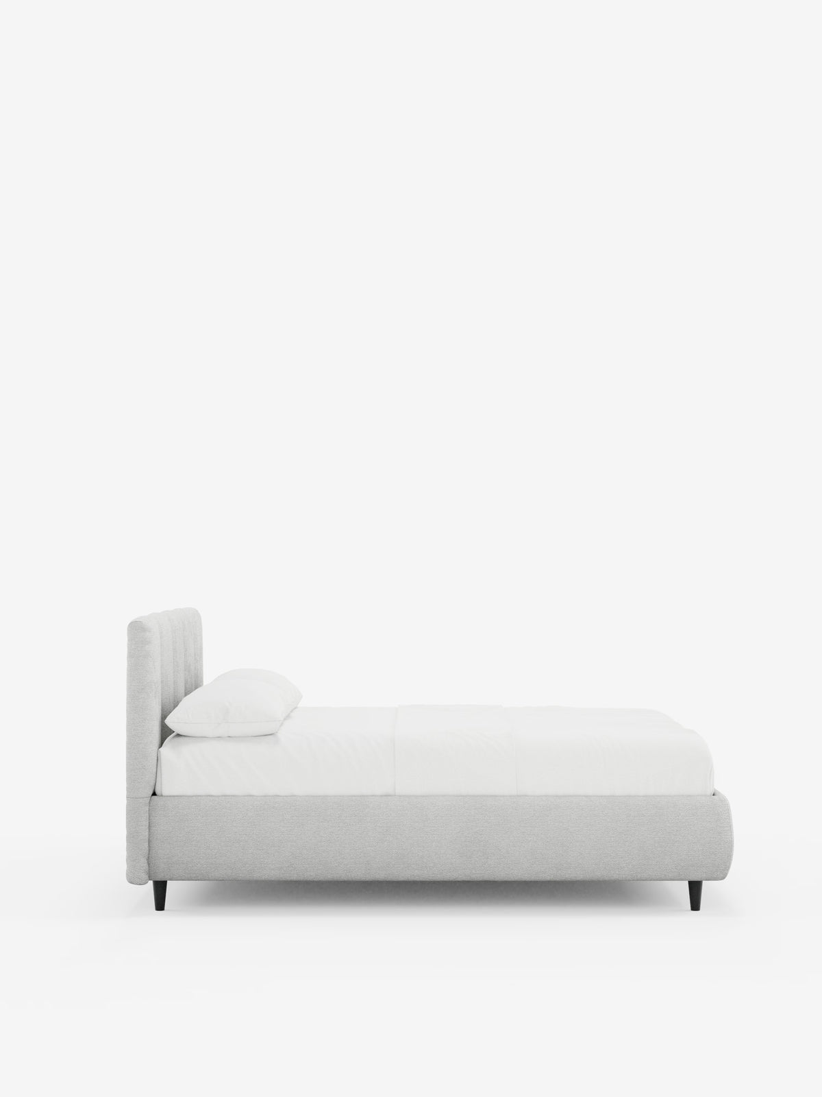 Vista laterale del letto imbottito ARKAM con contenitore e testiera a lavorazione verticale di Letti.store, caratterizzato da una struttura imbottita grigio chiaro certificata Oeko-Tex®, gambe basse nere e una testiera alta imbottita con dettagli verticali. Il letto è abbinato a biancheria da letto bianca e a un unico cuscino bianco, su uno sfondo bianco a tinta unita. L’effetto complessivo è minimalista e chic, con sottili elementi di design in stile shabby chic.