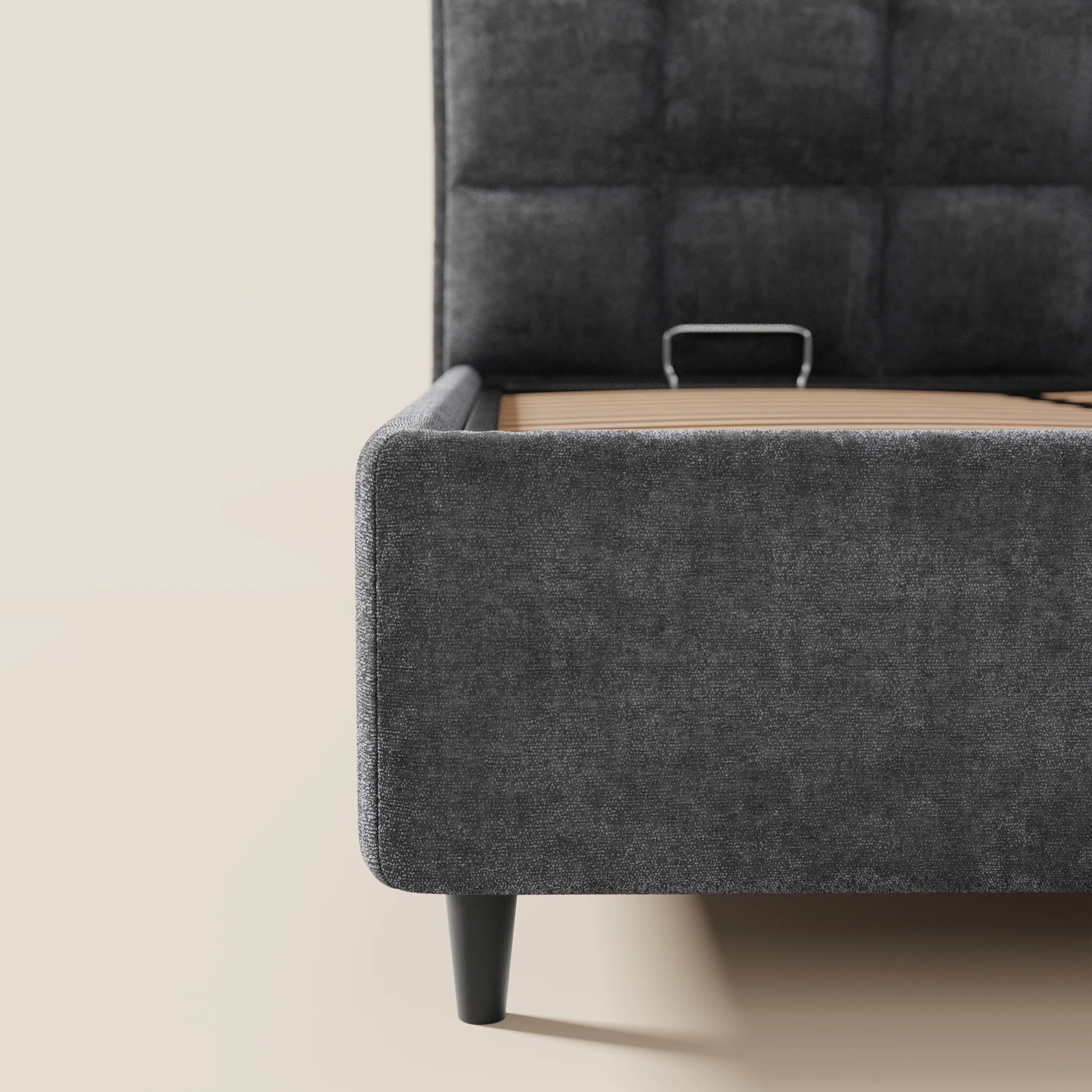 Primo piano del letto imbottito AURO di Letti.store con testiera alta capitonné in ciniglia Oeko-Tex® grigio scuro, gambe affusolate nere, sponda laterale bassa e base in legno a vista — materasso non incluso — su uno sfondo beige chiaro.