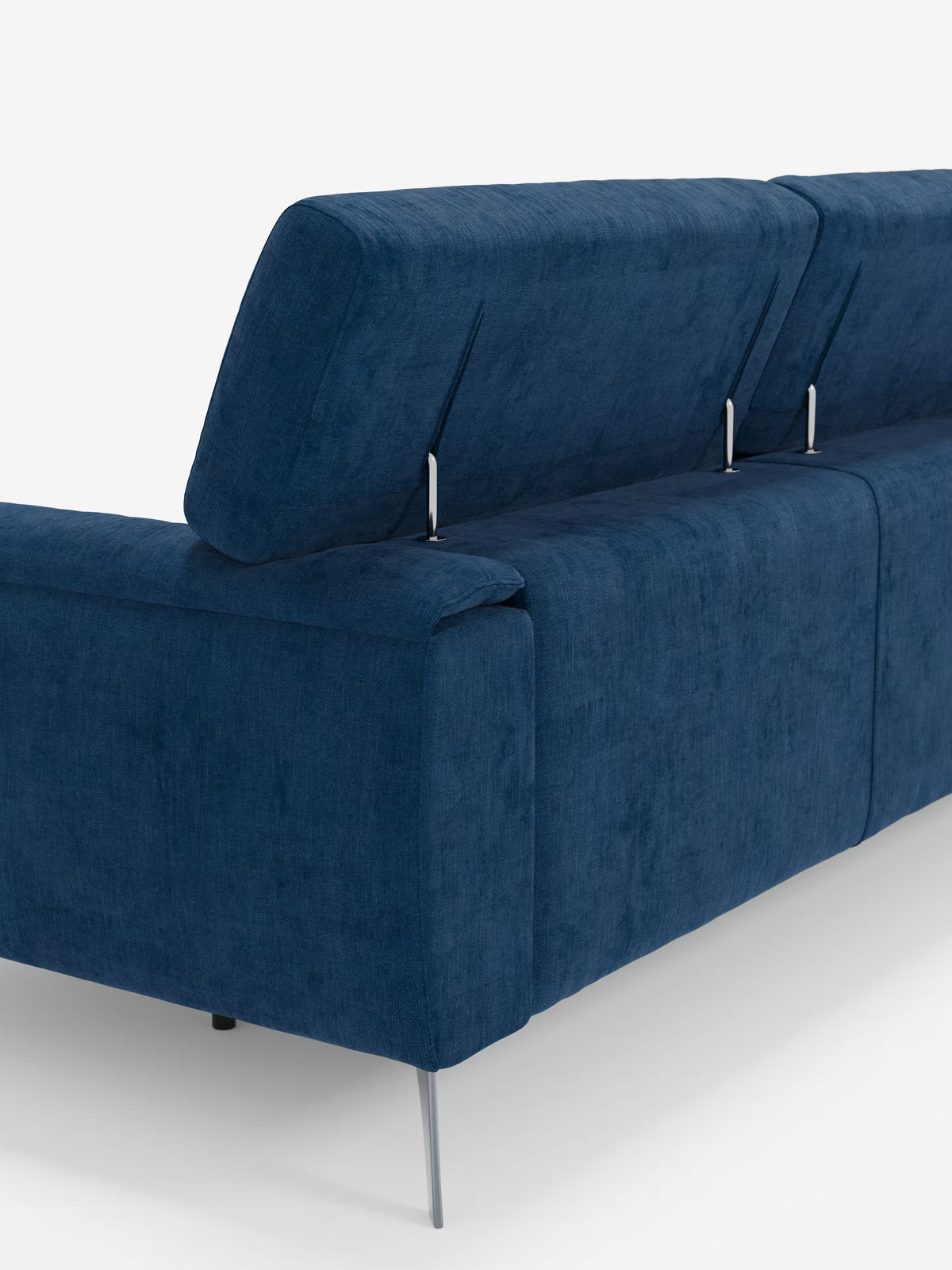 Un divano Caravaggio blu in stile contemporaneo a 4 posti con tre sedute scorrevoli di Divani.Store, rivestito in tessuto T31 antimacchia, dotato di poggiatesta reclinabili e gambe sottili in metallo. Lo schienale presenta tre poggiatesta segmentati e regolabili, sostenuti da eleganti elementi metallici. Sullo sfondo bianco a tinta unita, spicca l’elegante design di questo divano moderno.