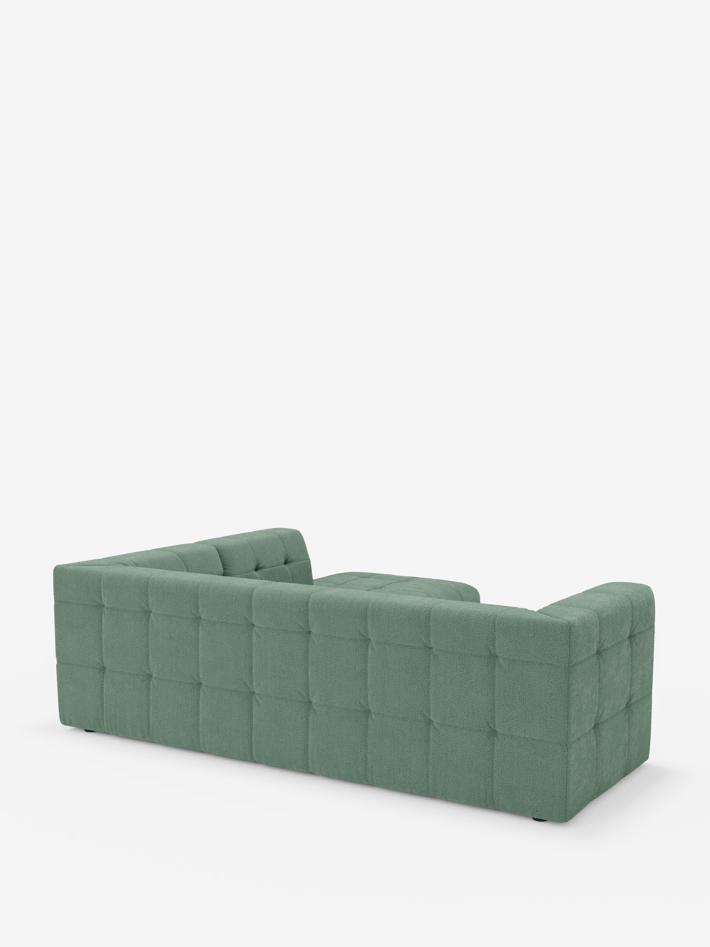 Un divano angolare componibile e modulare Mosaic, moderno e di colore verde, in bouclé: capitonné e design in tessuto smacchiabile T21 di Divani.Store, è raffigurato di spalle su uno sfondo bianco. Il divano presenta cuscini quadrati, braccioli bassi e un morbido rivestimento in bouclé dal design squadrato e contemporaneo.