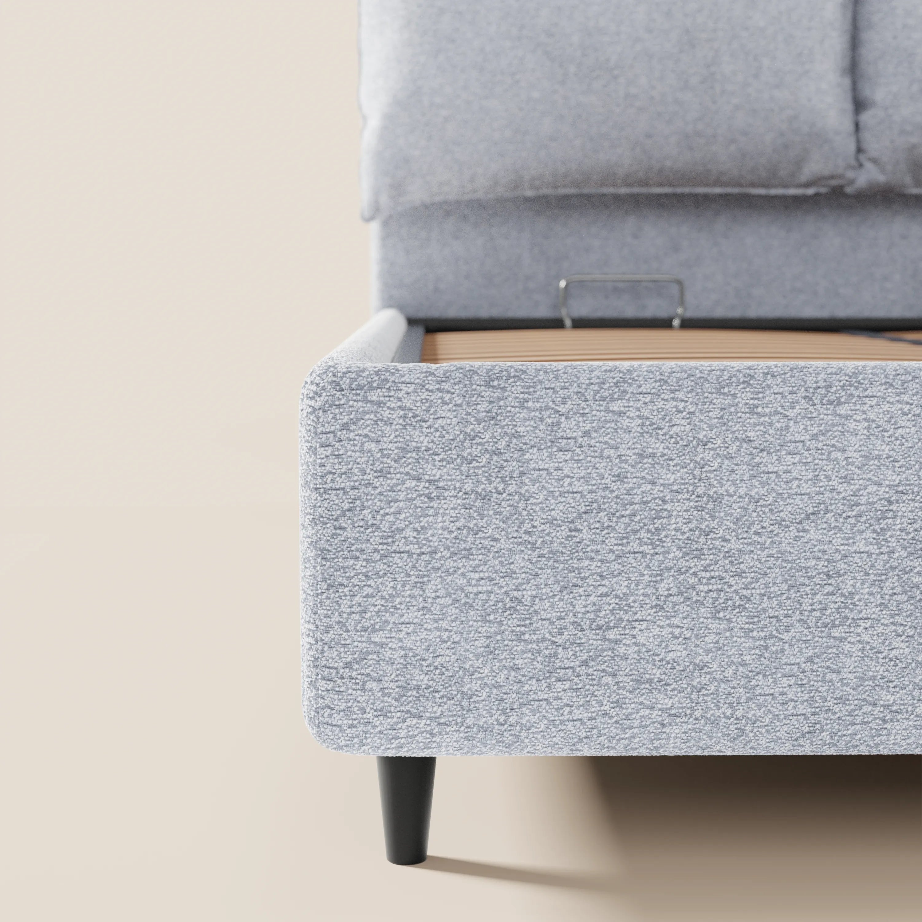 Un primo piano del letto imbottito ZAYRON di Letti.store, realizzato in tessuto grigio chiaro certificato Oeko-Tex®, con rivestimento testurizzato, gambe nere, dettaglio della rete a doghe e cuscini regolabili, ripreso su uno sfondo neutro.