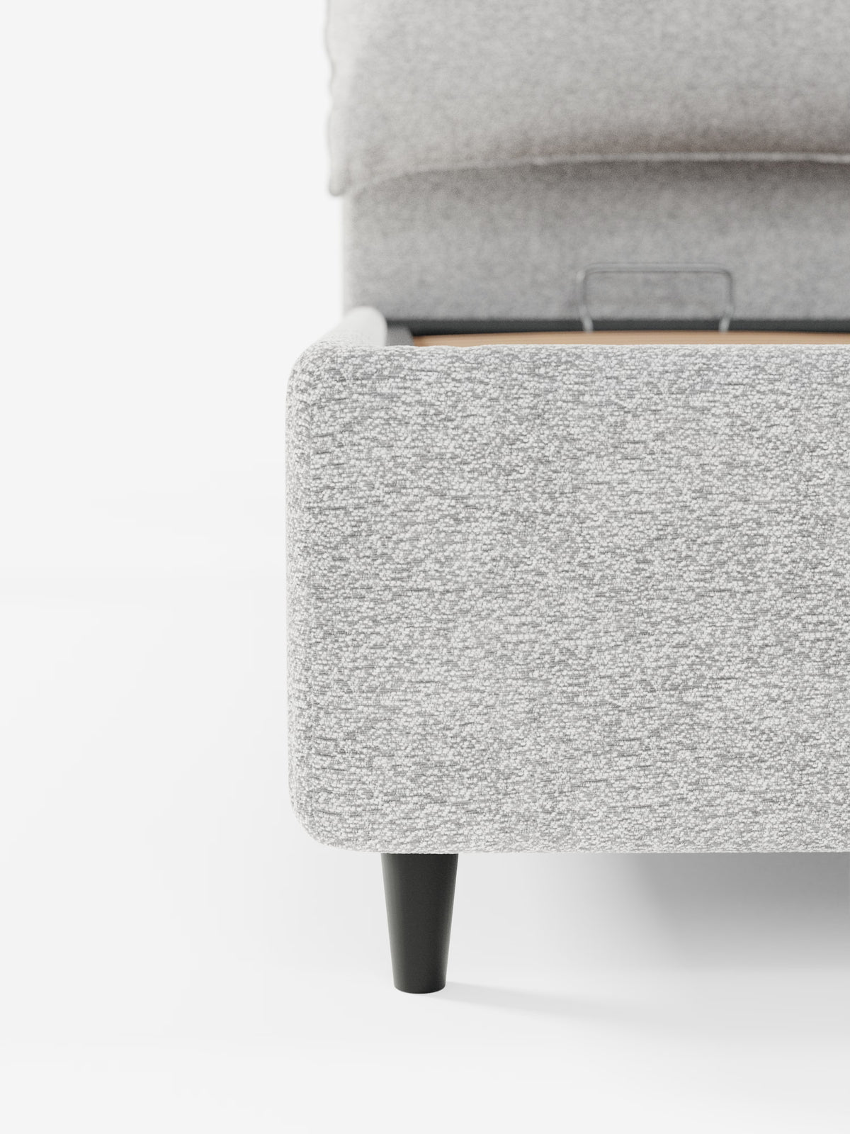Primo piano dell'angolo del letto imbottito ZAYRON con contenitore e morbidi cuscini regolabili di Letti.store, caratterizzato da un moderno tessuto grigio chiaro certificato Oeko-Tex®, una gamba affusolata nera e doghe in legno parzialmente visibili. Lo sfondo bianco minimalista ne esalta il design pulito e contemporaneo.