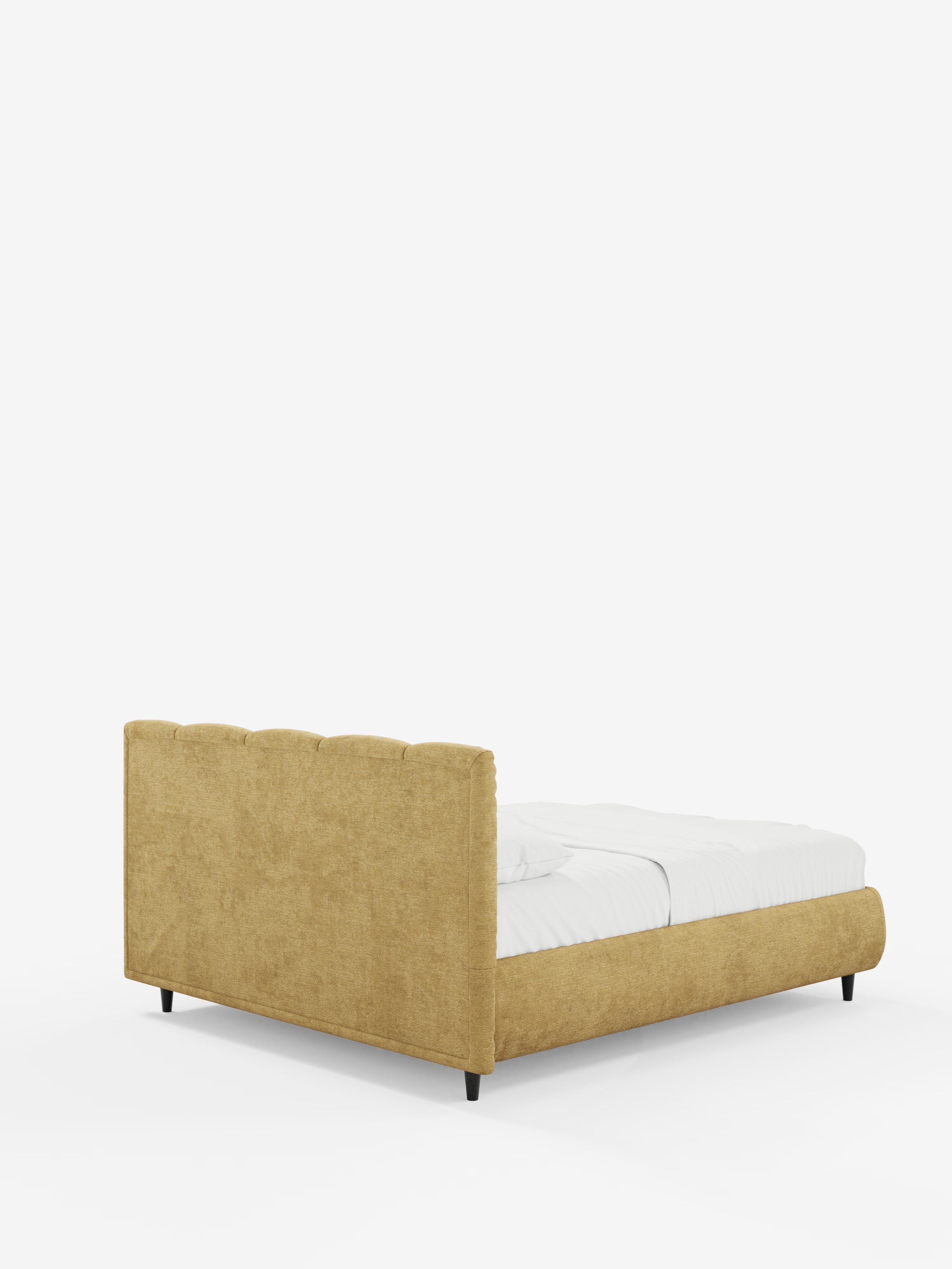Un letto ARKAM giallo senape imbottito con contenitore e testiera a lavorazione verticale di Letti.store, caratterizzato da una pediera bassa e rivestito con biancheria da letto bianca. Il letto in stile shabby-chic, realizzato in tessuto certificato Oeko-Tex®, poggia su quattro gambe corte e scure ed è fotografato da una prospettiva posteriore obliqua su uno sfondo bianco a tinta unita.