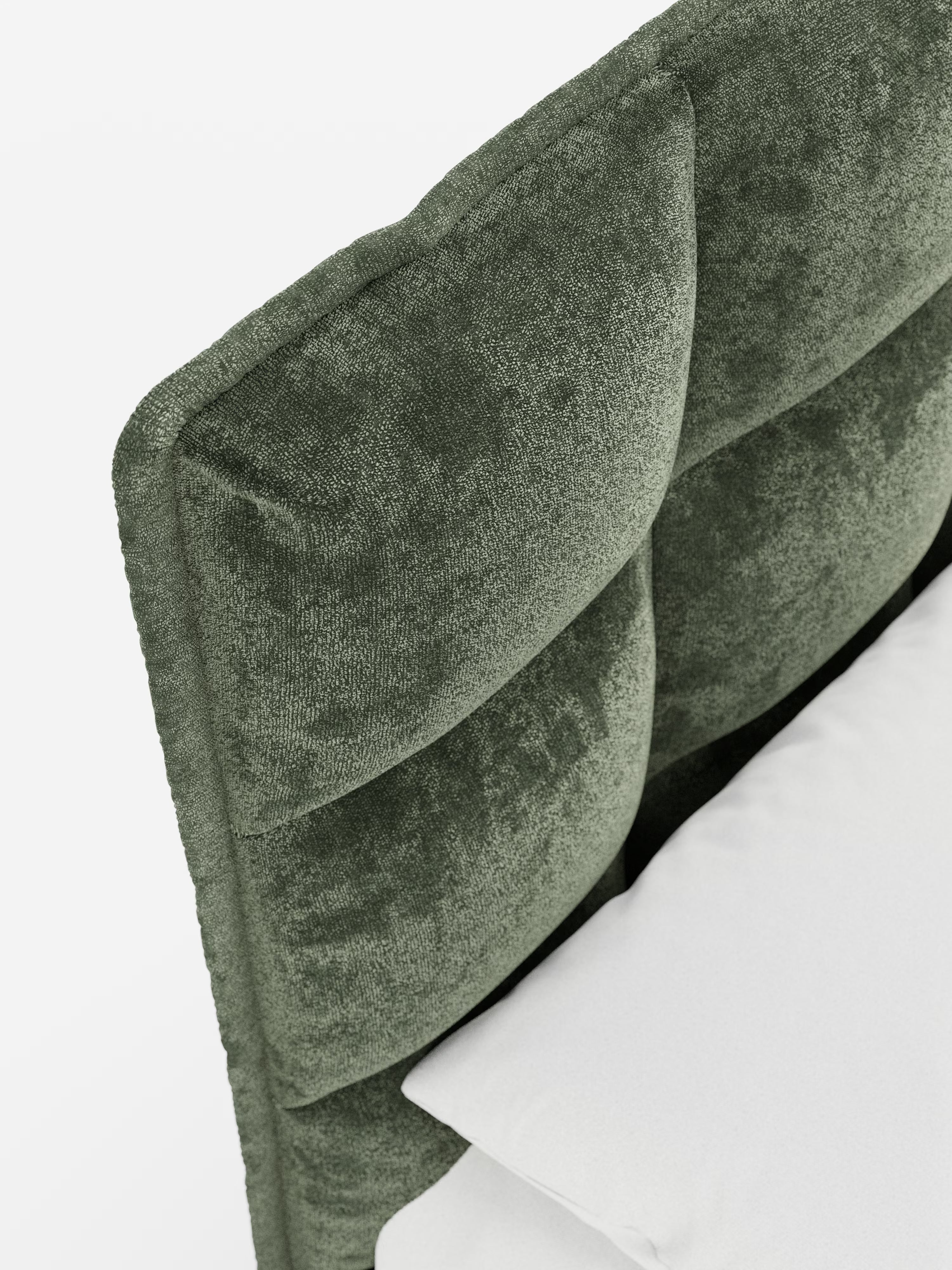 Primo piano del letto imbottito AURO di Letti.store, caratterizzato da un’alta testiera capitonné trapuntata, realizzata in ciniglia verde intenso certificata Oeko-Tex®. Il rivestimento in ciniglia testurizzata presenta un aspetto morbido e vellutato e un design angolare e accogliente. In basso a destra si intravede parte di un cuscino bianco e di un materasso su uno sfondo semplice e luminoso.