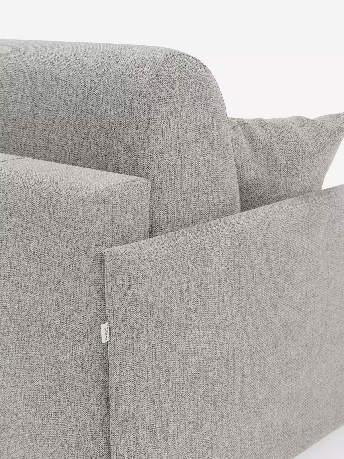 Un primo piano del divano letto matrimoniale sfoderabile Evans di Divani.Store mette in risalto il suo rivestimento in tessuto T23 grigio chiaro, moderno e resistente alle macchie, dalle linee pulite, evidenziando i braccioli, lo schienale e un cuscino decorativo abbinato. È visibile la trama dettagliata del tessuto e una piccola etichetta bianca è applicata alla cucitura del bracciolo. Il design compatto presenta anche un pratico vano portaoggetti per i cuscini.