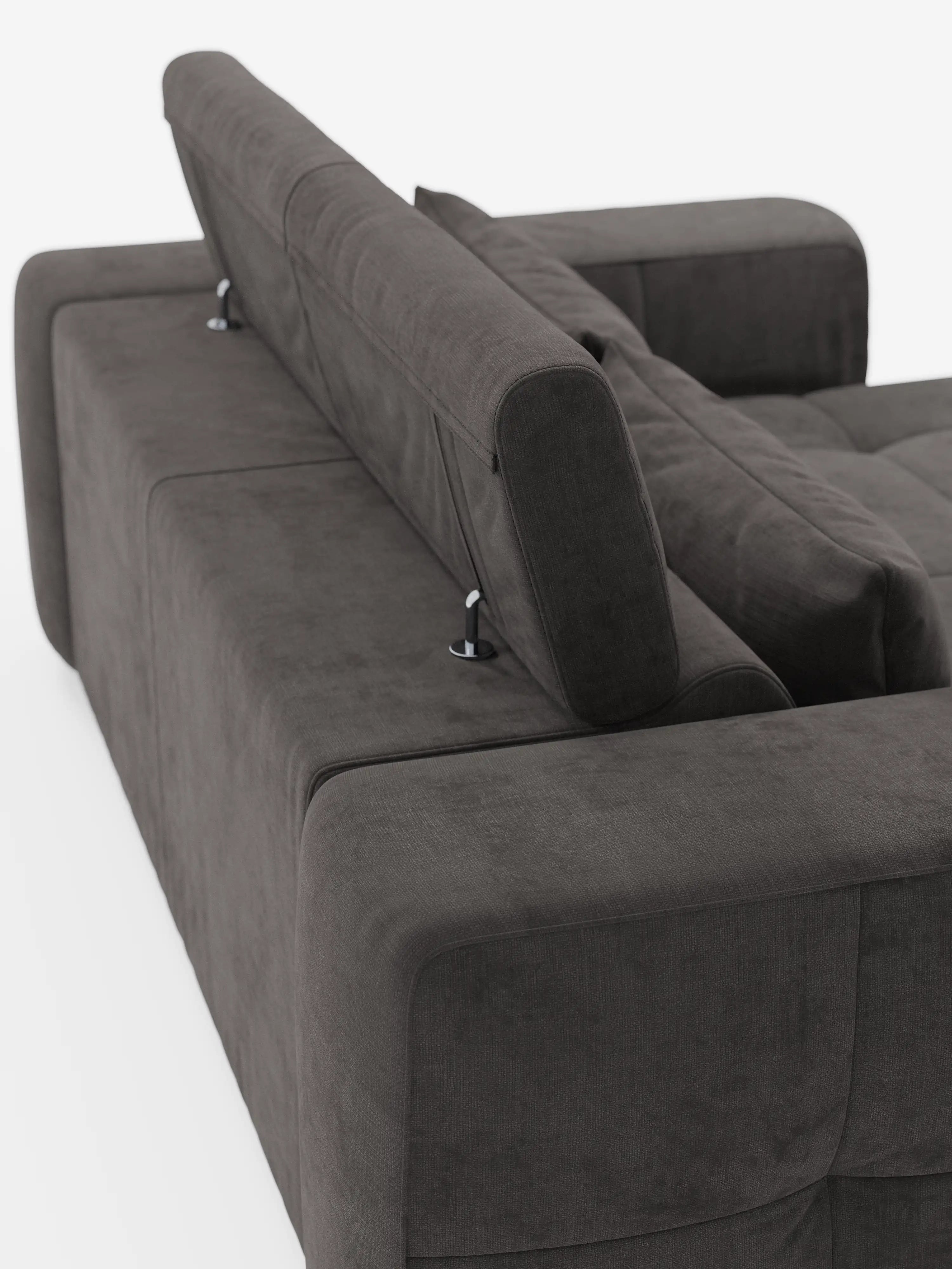 Una vista ravvicinata e obliqua del divano Monarch con relax elettrico per l’allungamento delle sedute e poggiatesta reclinabile in morbido tessuto smacchiabile T31 di Divani.Store, nella versione grigio scuro, ne mette in risalto il lussuoso rivestimento. Lo schienale e i braccioli, spessi e imbottiti, aggiungono comfort, mentre il poggiatesta reclinabile regolabile è sollevato per mostrare gli eleganti supporti in metallo argentato. Questo divano relax elettrico risalta su uno sfondo bianco a tinta unita.