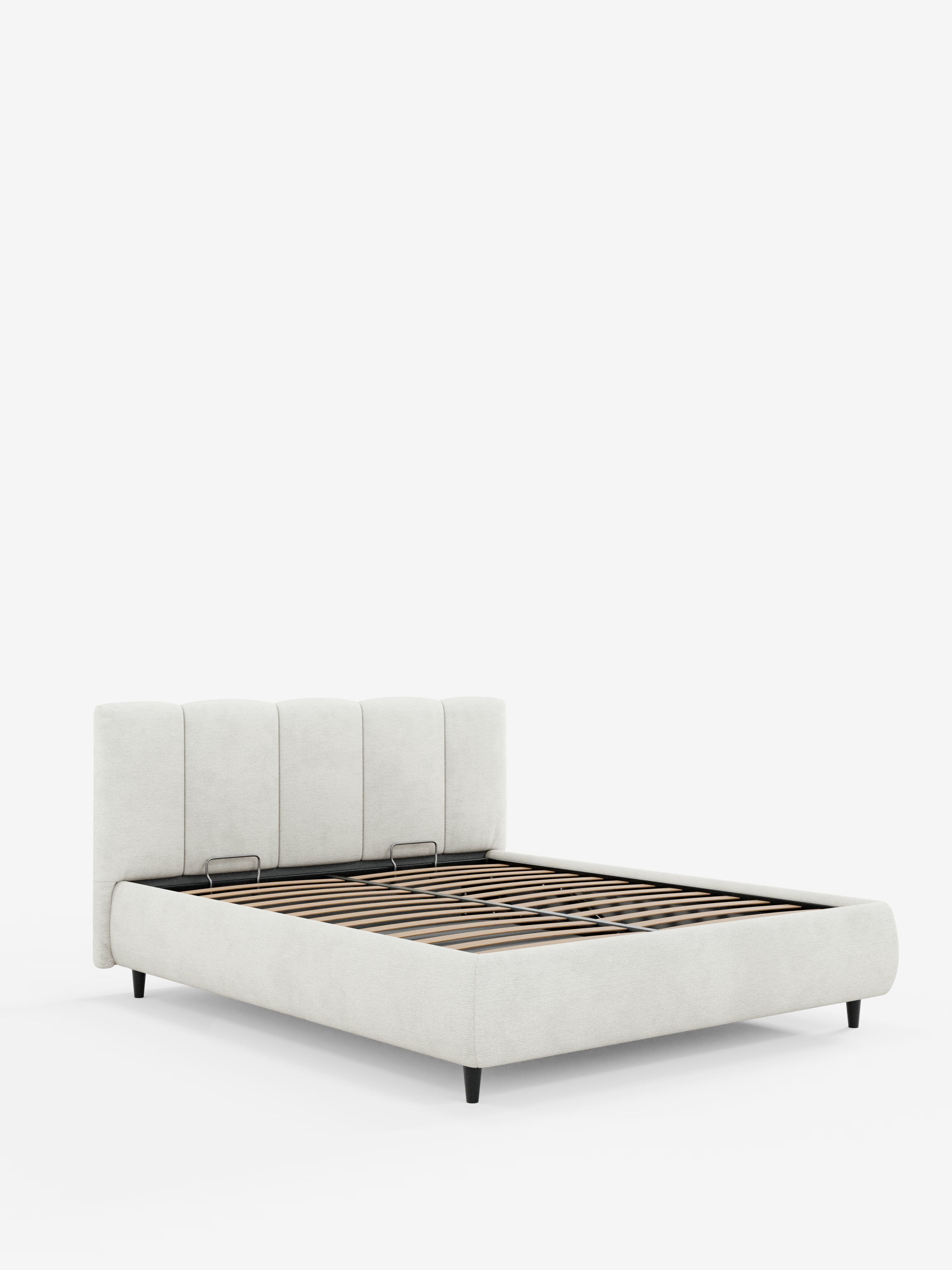 Il letto imbottito ARKAM di Letti.store è un letto a piattaforma in stile shabby chic con struttura in tessuto grigio chiaro certificato Oeko-Tex® e un'alta testiera imbottita caratterizzata da quattro pannelli verticali. È dotato di doghe in legno, gambe corte nere e un pratico vano contenitore. Presentato su uno sfondo bianco a tinta unita.