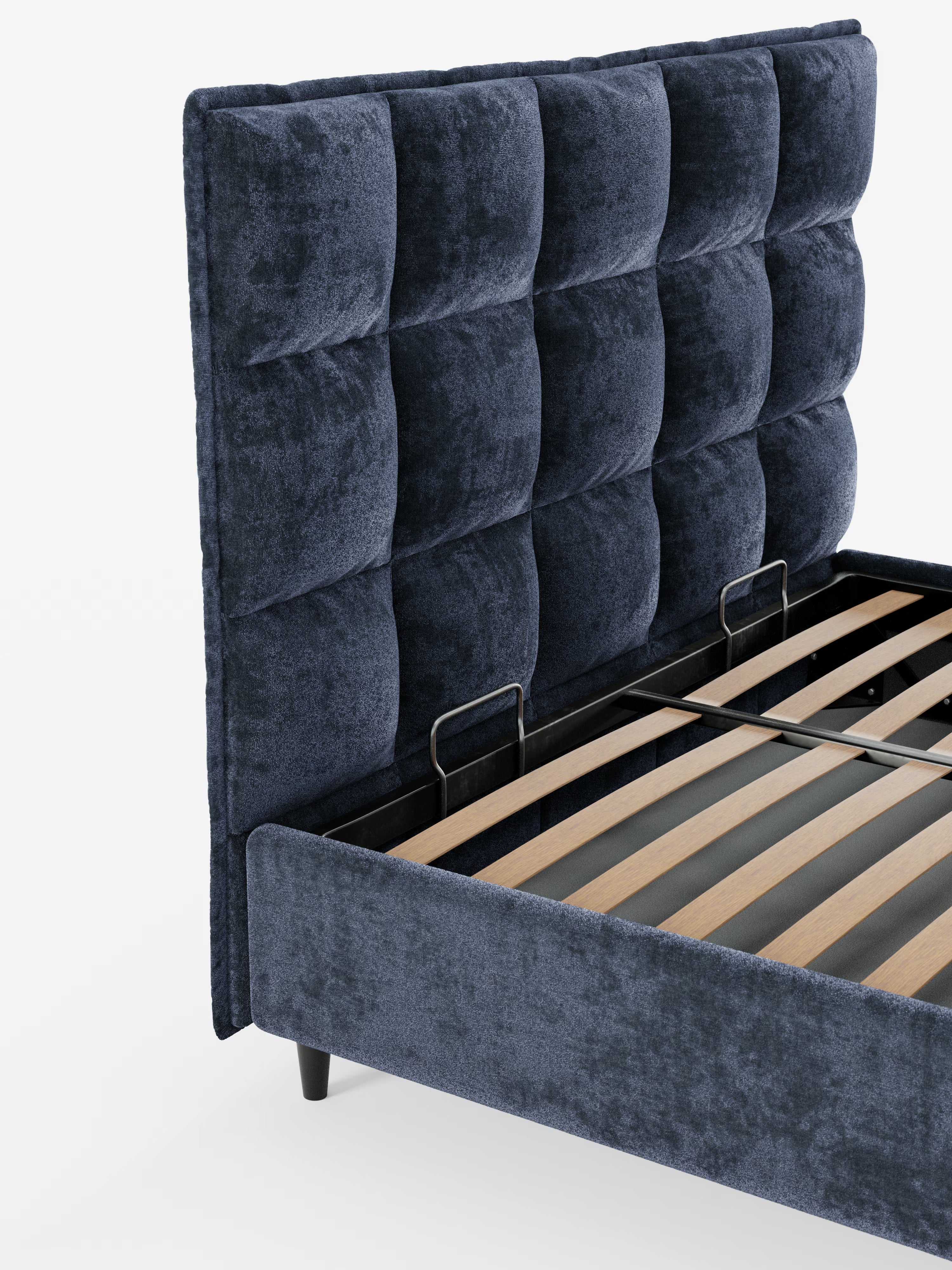 Un primo piano del letto imbottito con contenitore AURO di Letti.store, caratterizzato da un design moderno con una testiera alta e capitonné, rivestita in ciniglia blu navy certificata Oeko-Tex®. La struttura del letto è composta da robuste doghe in legno sostenute da travi metalliche a vista e poggia su corte gambe nere. In primo piano su uno sfondo bianco a tinta unita.