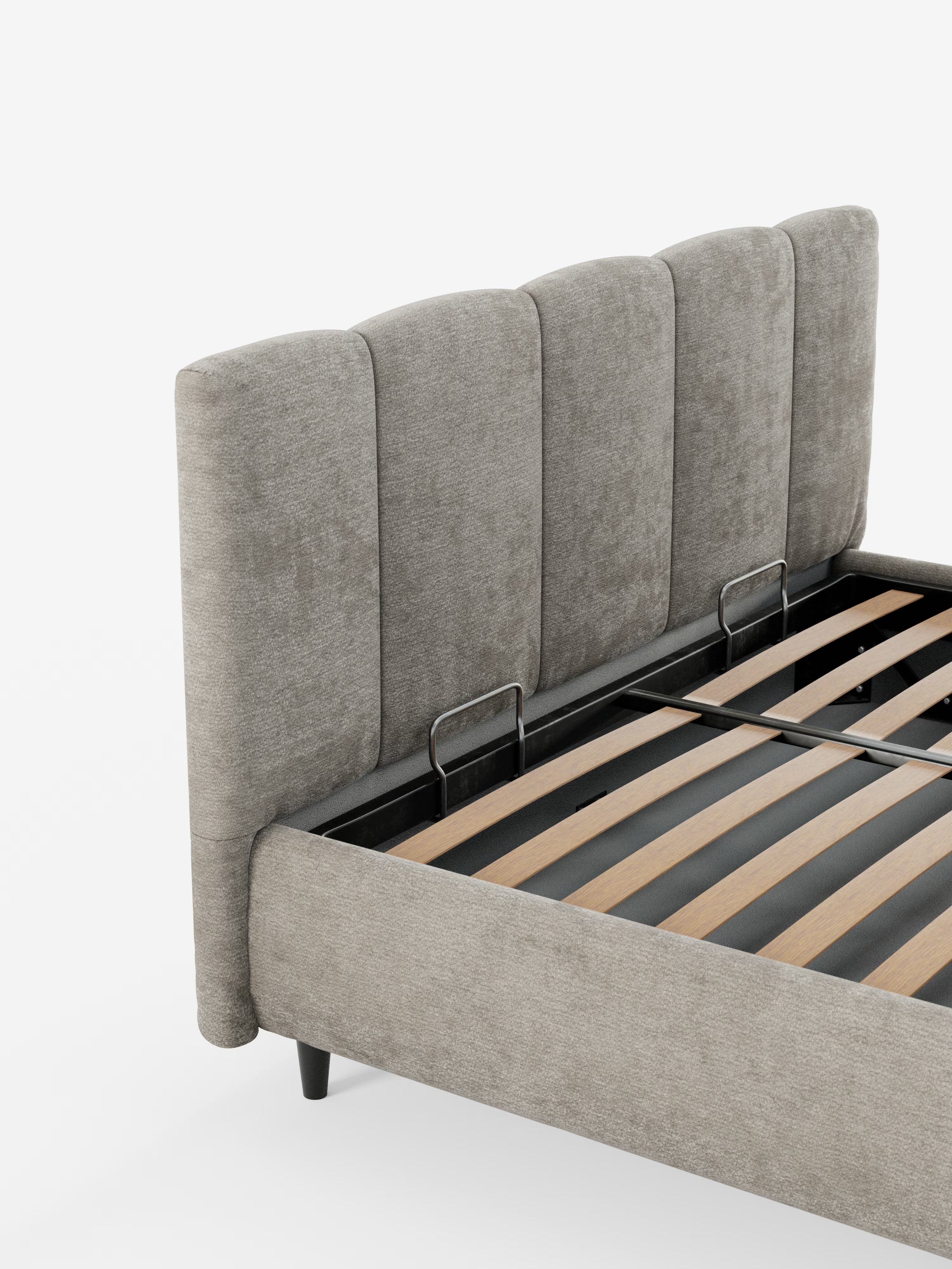 Un primo piano del letto imbottito ARKAM di Letti.store con contenitore e testiera a lavorazione verticale, caratterizzato da un’alta testiera grigia imbottita con pannelli verticali, rivestita in tessuto certificato Oeko-Tex® e dal design shabby chic. Sono visibili le doghe in legno e la struttura in metallo nero del letto, insieme a due staffe argentate. Lo sfondo è bianco.