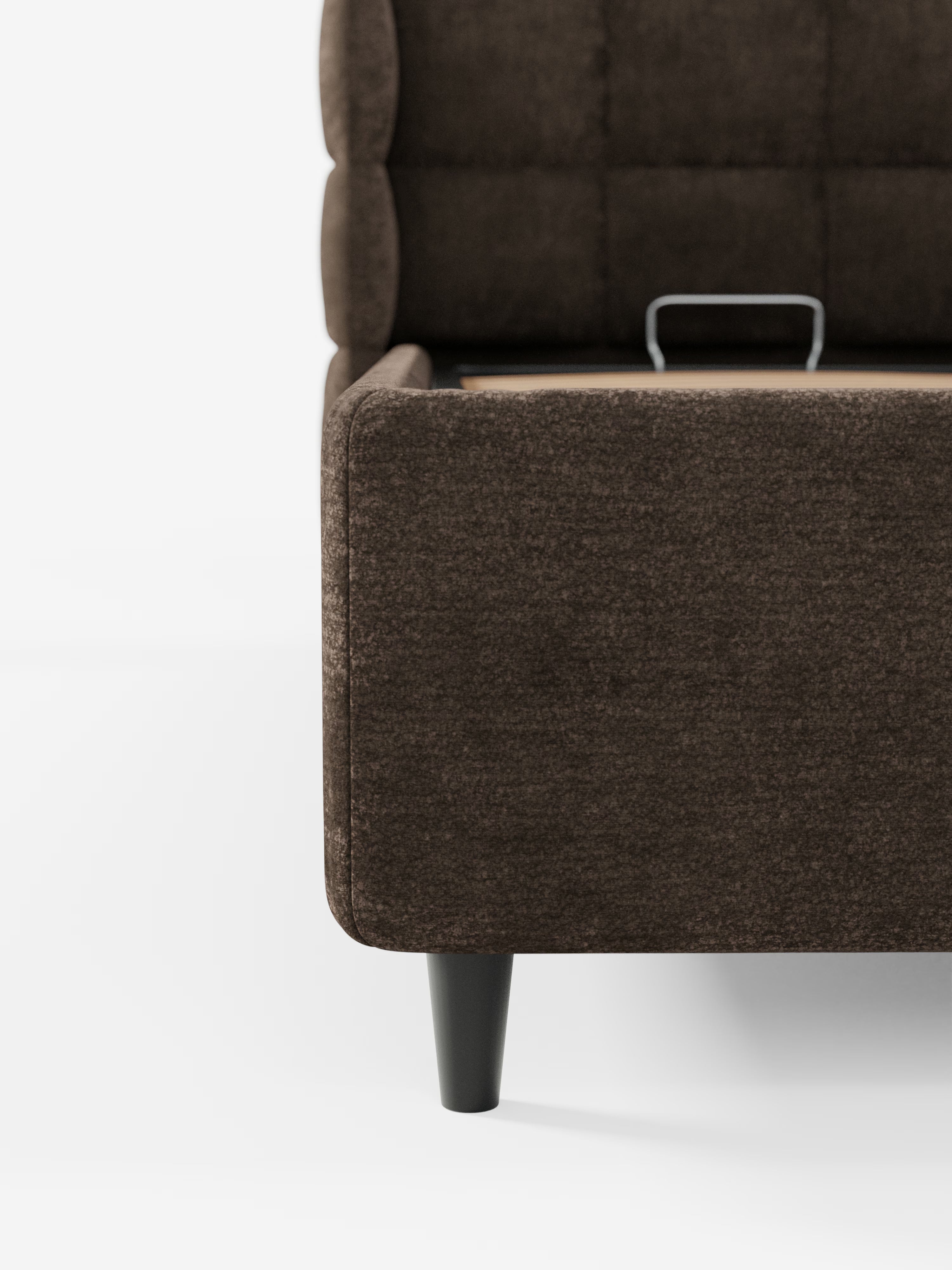 Primo piano del letto imbottito RAGNAR con vano contenitore e testiera capitonné avvolgente di Letti.store, elegantemente rivestito in tessuto marrone scuro certificato Oeko-Tex®. Il letto poggia su gambe nere corte e angolate, mentre una piccola maniglia metallica sul bordo superiore lascia intuire la presenza di un ampio vano contenitore all’interno della base. Immagine su sfondo bianco.