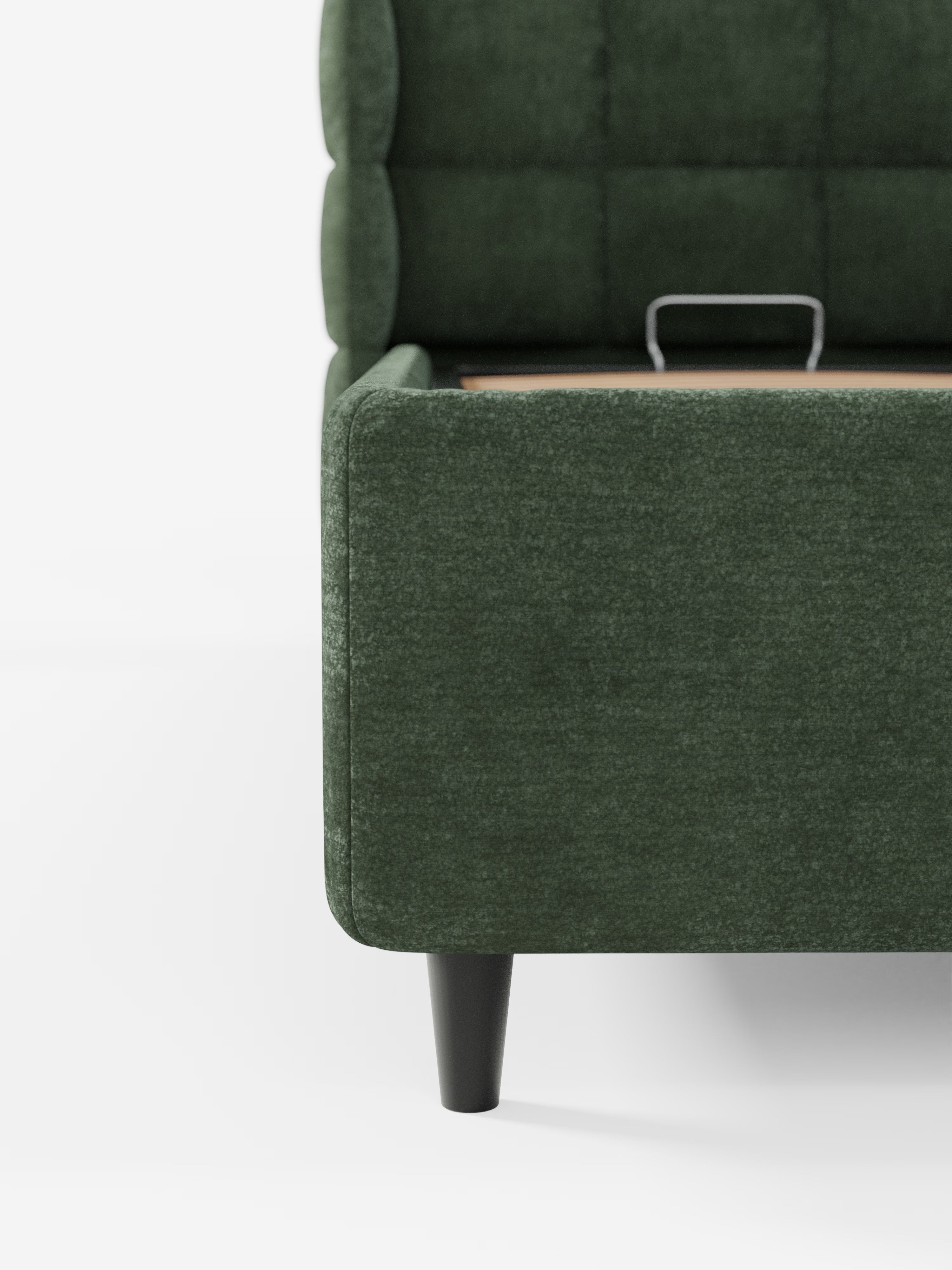 Primo piano del letto imbottito RAGNAR con vano contenitore e testiera capitonné avvolgente di Letti.store, caratterizzato da un elegante rivestimento verde scuro certificato Oeko-Tex®, gambe affusolate nere, una testiera capitonné trapuntata avvolgente e un vano contenitore parzialmente rialzato con una piccola maniglia metallica. Lo sfondo è bianco a tinta unita.