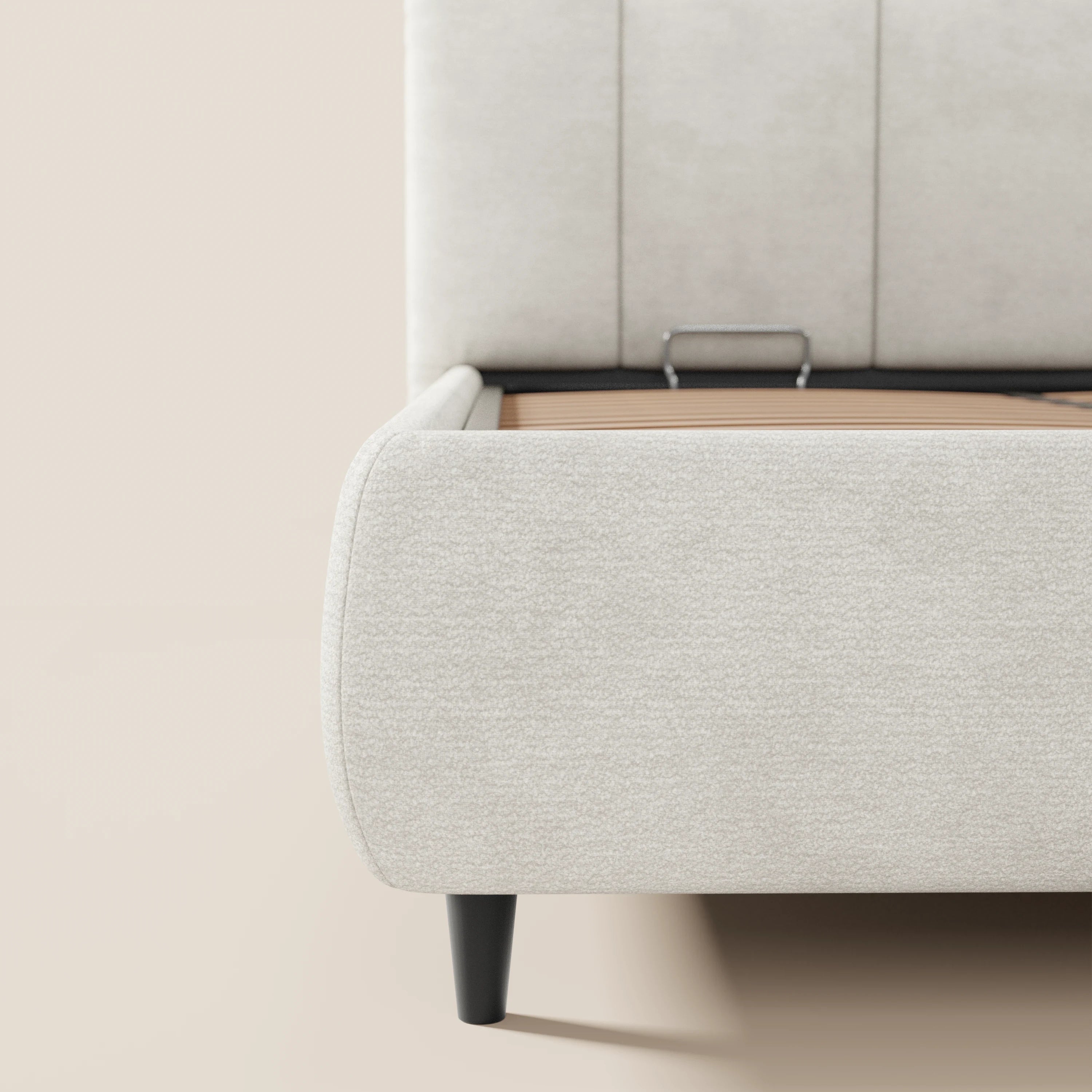 Primo piano dell'angolo del letto imbottito ARKAM con vano contenitore e testiera a lavorazione verticale di Letti.store, realizzato in tessuto certificato Oeko-Tex®, che ne evidenzia il bordo morbido, la gamba nera e le doghe in legno a vista con barra di sostegno in metallo all'interno del telaio.