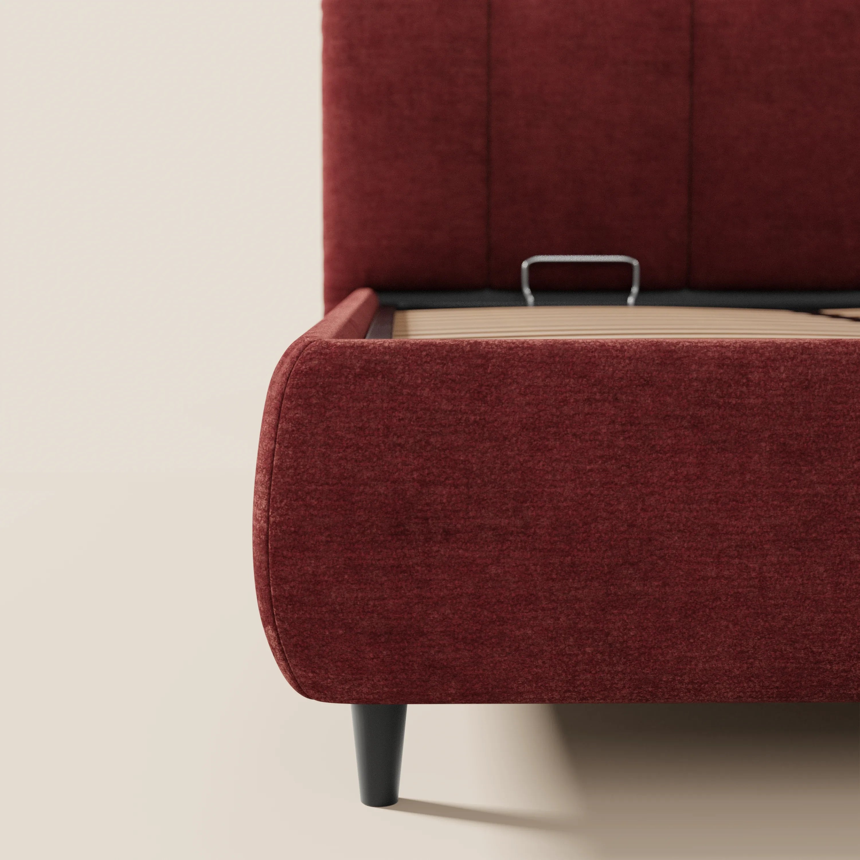 Vista parziale del letto imbottito ARKAM con vano contenitore e testiera a lavorazione verticale di Letti.store, in stile shabby chic, rivestito in tessuto rosso scuro certificato Oeko-Tex® con gambe affusolate nere. Presentato su un pavimento chiaro, in contrasto con una parete bianco sporco.