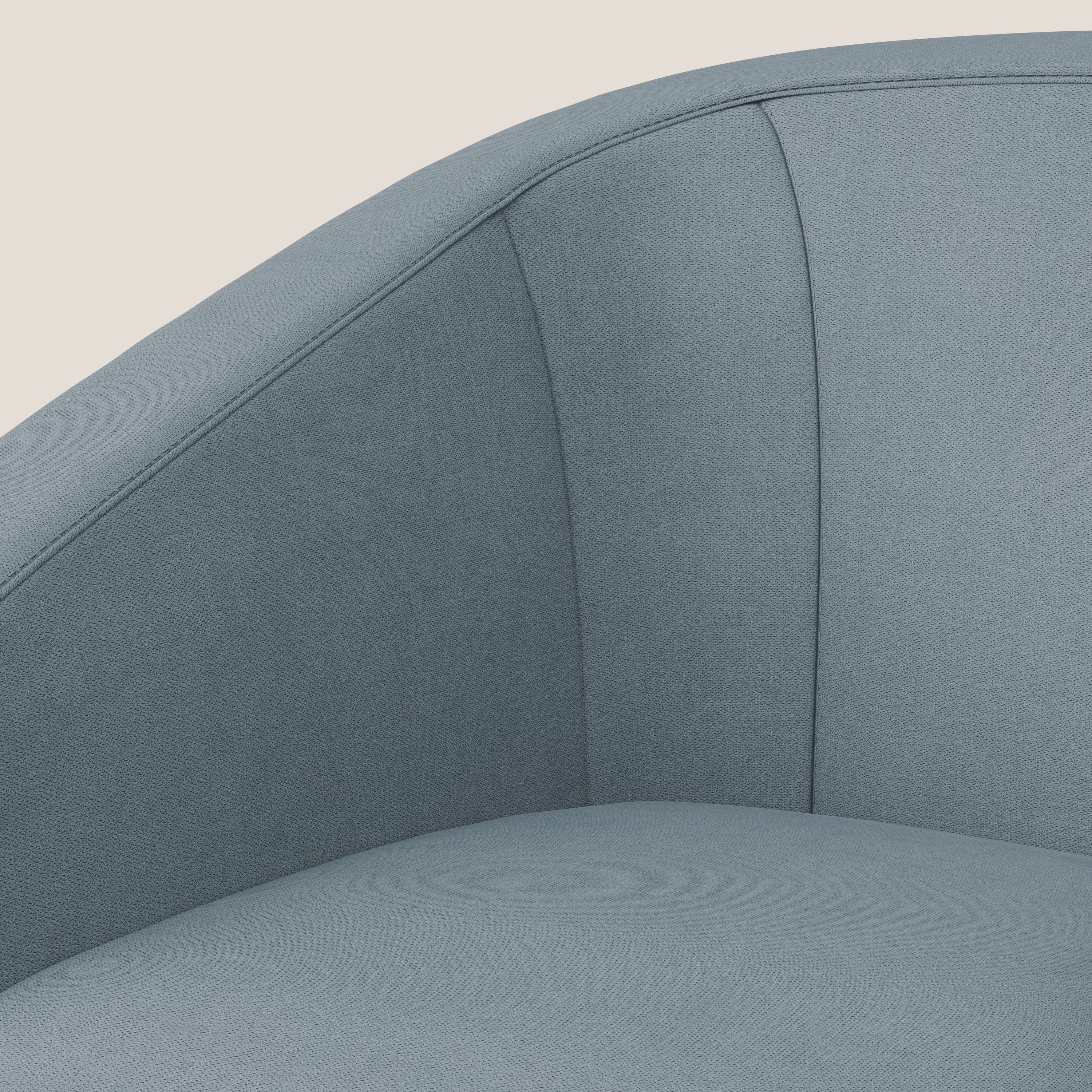 Primo piano della Poltroncina Sally in tessuto morbido impermeabile T02 carta da zucchero di Divani.Store, caratterizzata da schienale e bracciolo lisci e curvi, cuciture sottili e una morbida seduta imbottita su uno sfondo bianco sporco.