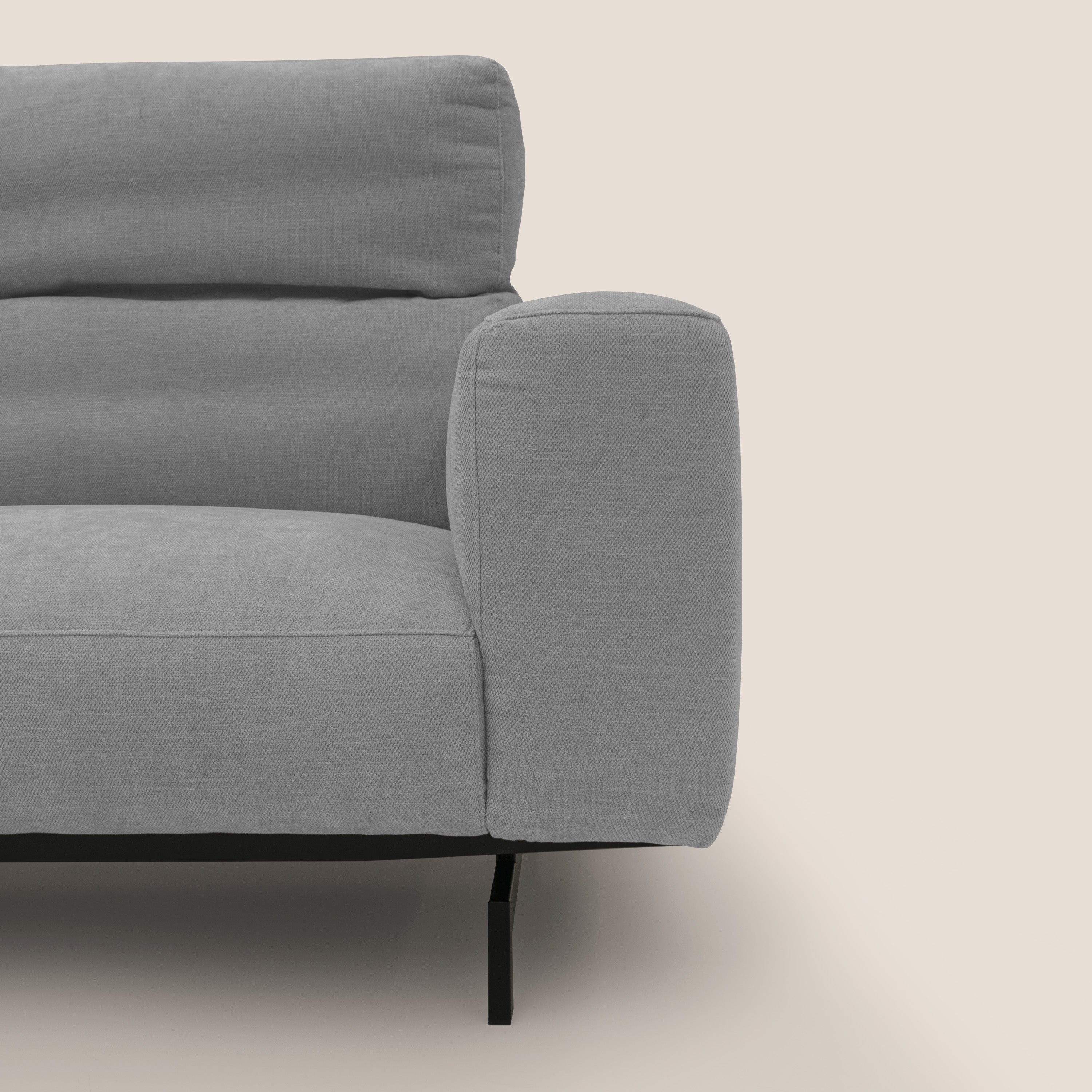 Primo piano del divano Sakura in piuma d'oca angolare REVERSIBILE di Divani.Store, in morbido tessuto fiammato impermeabile T14 grigio chiaro, con cuscini trapuntati orizzontali e gambe nere sottili su sfondo bianco.