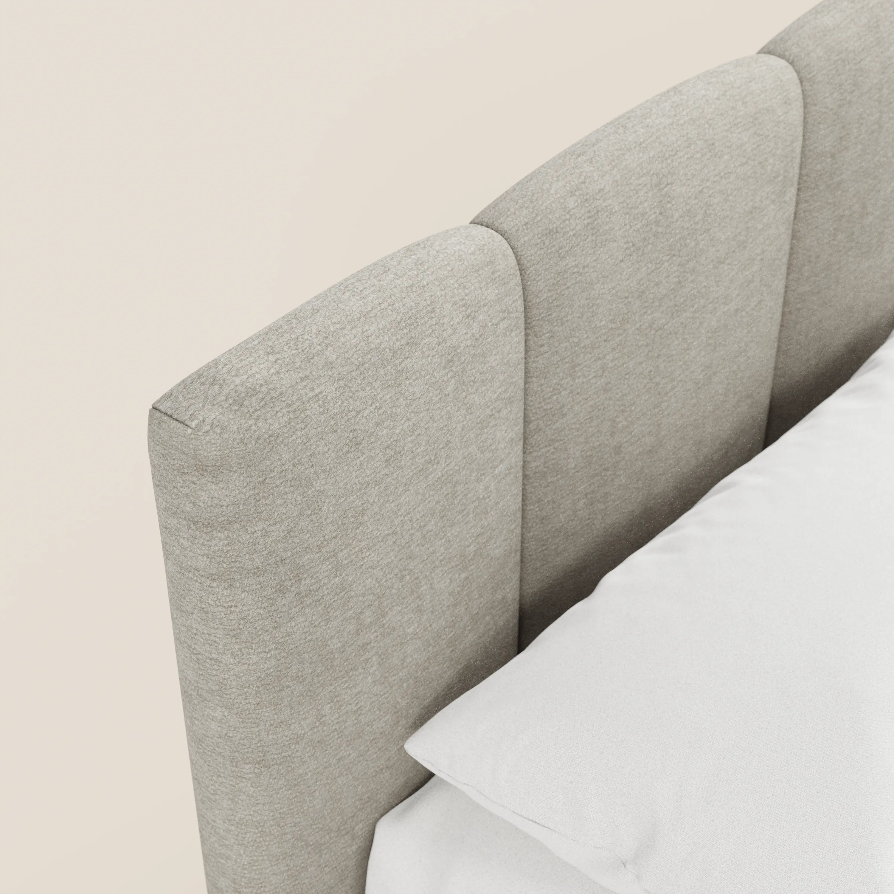 Primo piano del letto imbottito ARKAM di Letti.store, caratterizzato da una testiera in stile shabby chic con lavorazione verticale in tessuto grigio chiaro certificato Oeko-Tex®, con biancheria da letto bianca che ne esalta il design elegante e contemporaneo su uno sfondo chiaro.