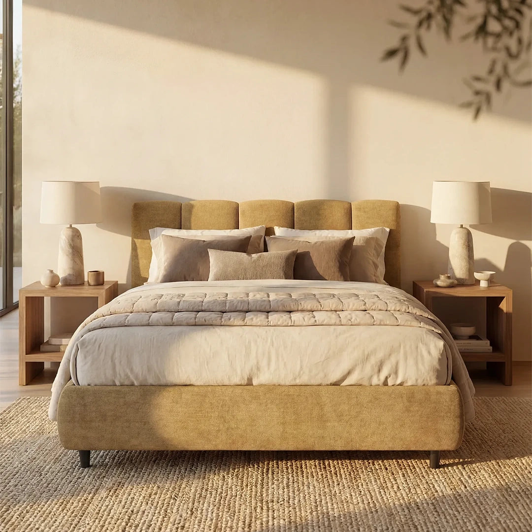 Un'accogliente camera da letto ospita il letto imbottito ARKAM con contenitore e testiera verticale di Letti.store, rivestito con biancheria da letto e cuscini dai toni neutri. Comodini in legno e lampade dall'effetto pietra fiancheggiano il letto, mentre la luce del sole riscalda un tappeto dalla trama ricca, creando un elegante look shabby chic.