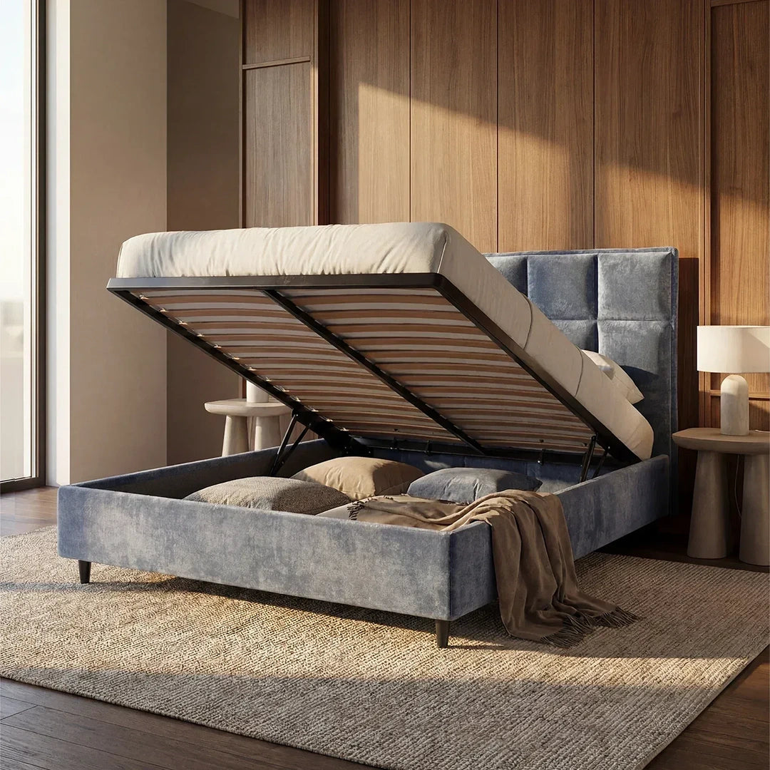 Una camera da letto moderna è arredata con il letto imbottito AURO con vano contenitore e testiera capitonné alta in ciniglia Oeko-Tex® di Letti.store, qui raffigurato con il materasso sollevato per rivelare lo spazio dedicato a cuscini e coperte. Lo spazio presenta pareti rivestite in legno e ampie finestre inondate di luce naturale.