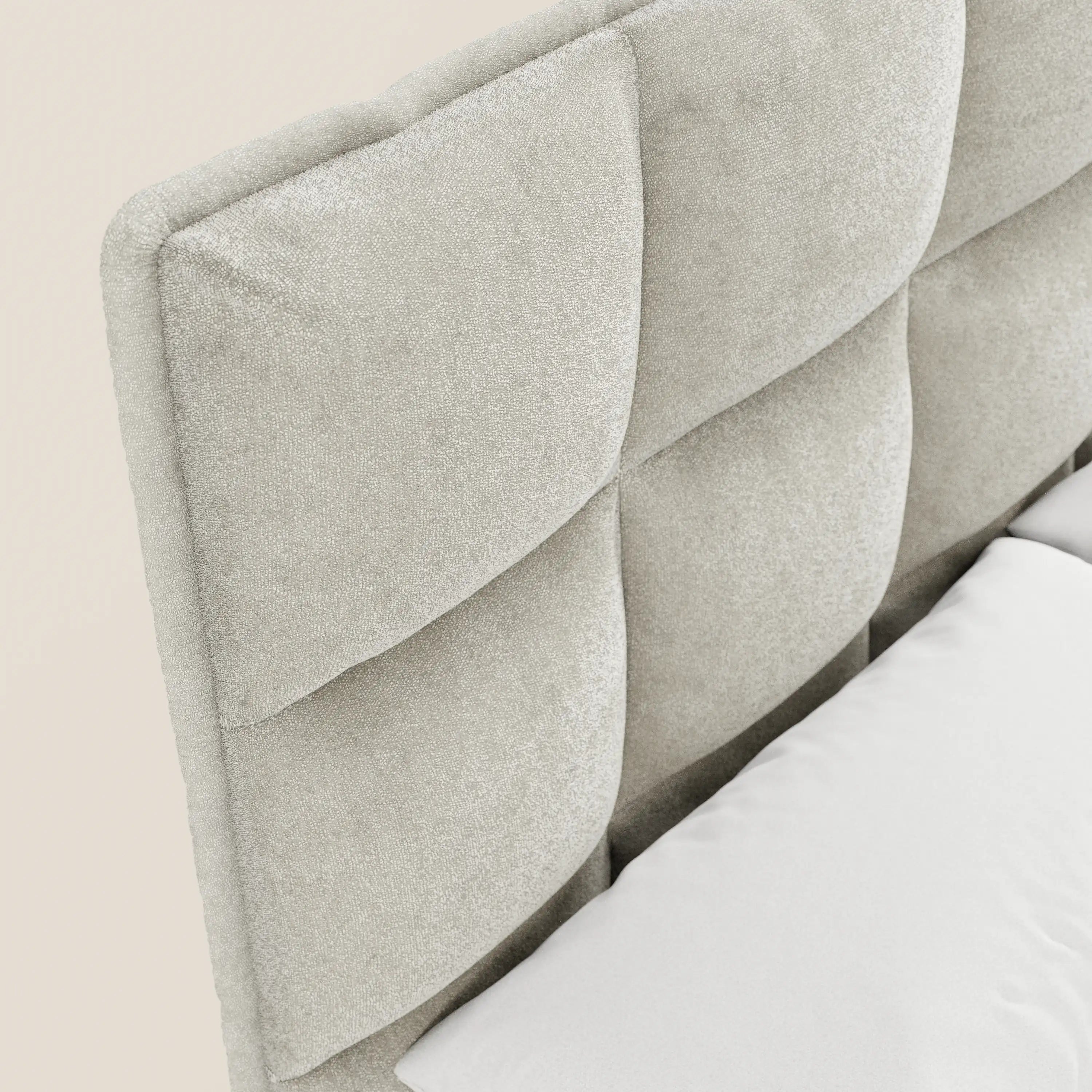 Primo piano del letto imbottito AURO con vano contenitore e testiera alta capitonné in ciniglia Oeko-Tex® di Letti.store, caratterizzato da una finitura effetto velluto beige chiaro con motivo geometrico; in basso a destra è visibile un cuscino bianco.