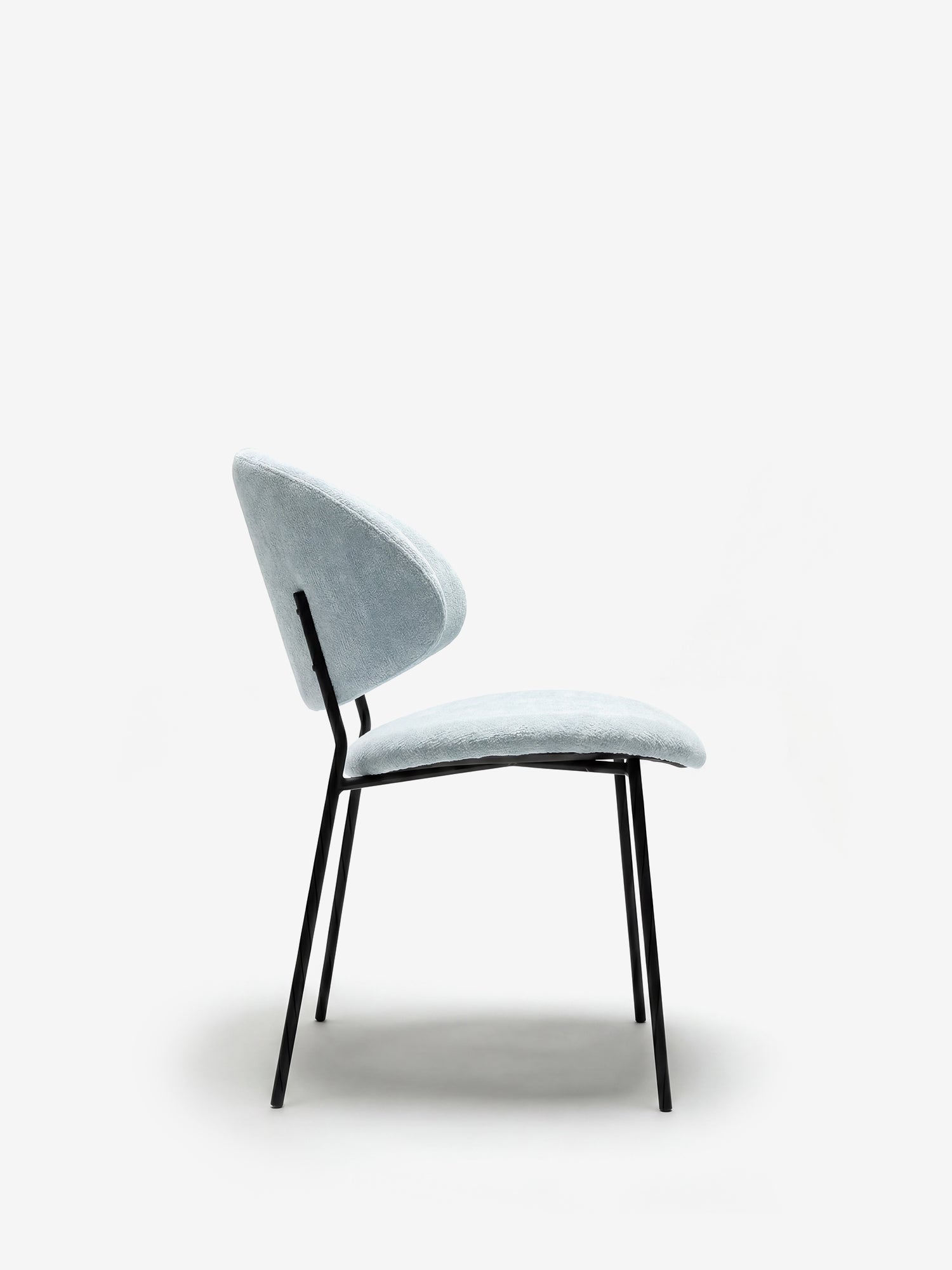 Sedia Bruma di Divani.Store: elegante tessuto goffrato, gambe in metallo nero, design minimalista e schienale avvolgente, raffigurata di profilo su sfondo bianco.