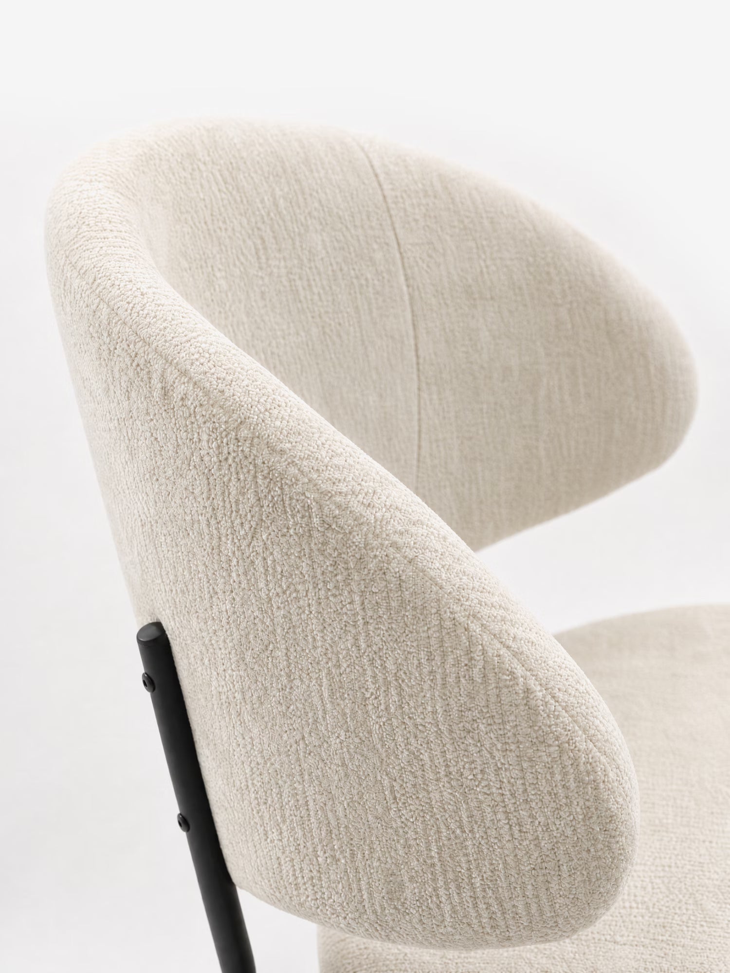 Un primo piano della sedia Bruma di Divani.Store, caratterizzata da un elegante tessuto goffrato, uno schienale avvolgente e gambe in metallo nero, ne mette in risalto il design minimalista su uno sfondo bianco a tinta unita.