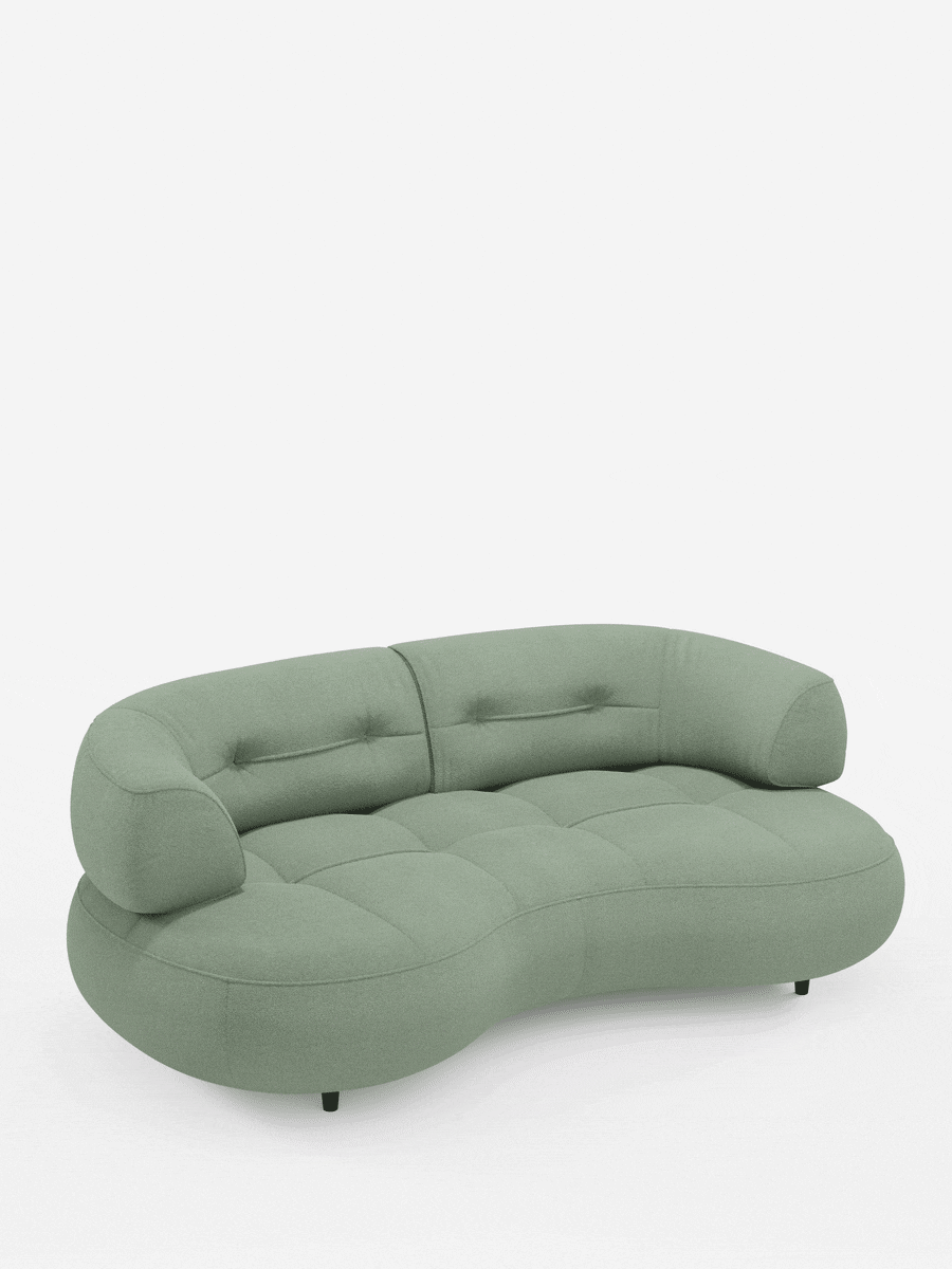 Un divano curvo a fagiolo a 3 posti “Croissant” color verde salvia, con schienali traslanti in morbido tessuto effetto cotone smacchiabile T33, caratterizzato da una forma curva, seduta trapuntata, schienali spessi e arrotondati e piccole gambe nere su sfondo bianco.