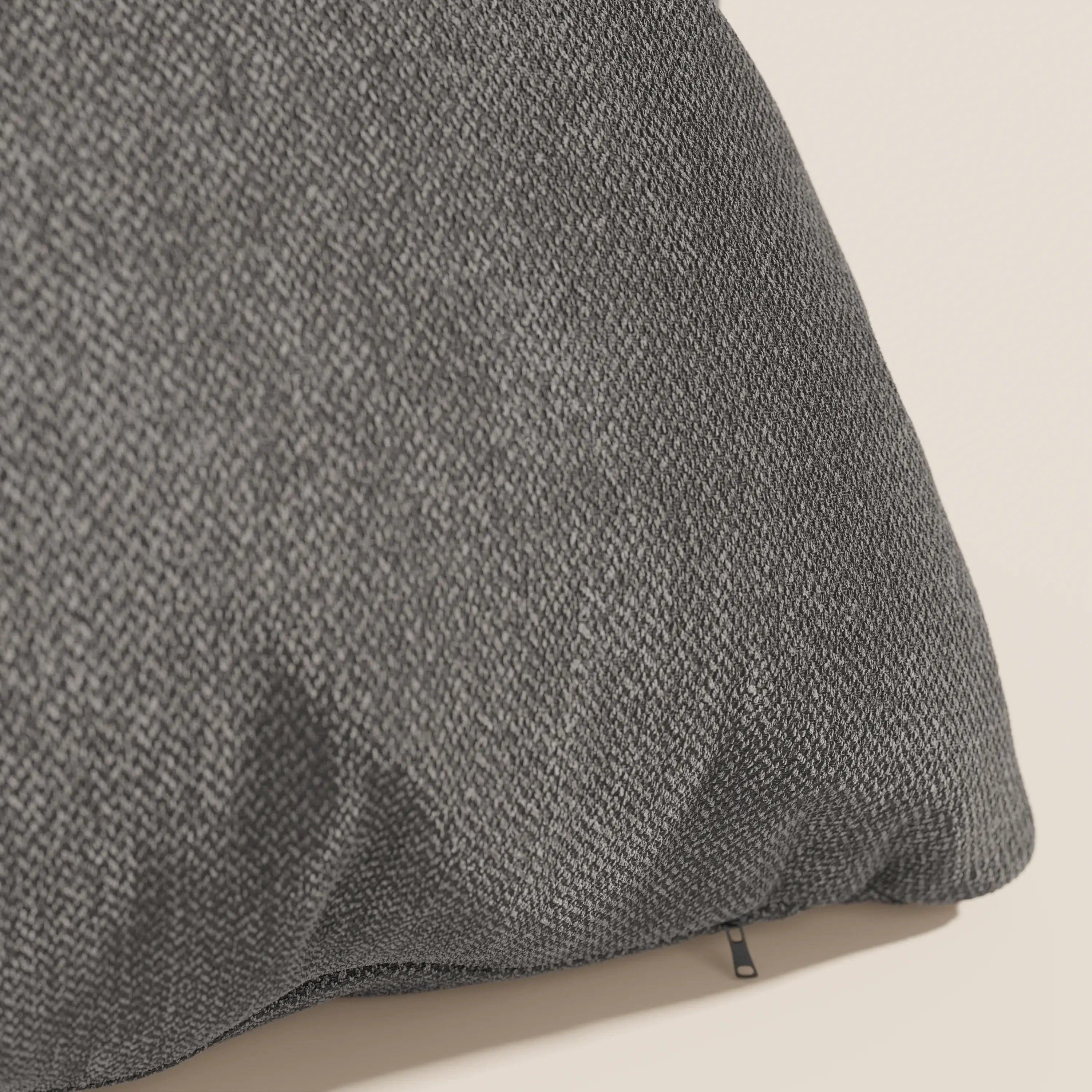 Un primo piano del cuscino Sogno di Divani.Store in tessuto antracite SMACCHIABILE T05 mostra la sua trama morbida e sottile e una discreta cerniera nera, con una parte di questo elegante cuscino su uno sfondo beige chiaro.