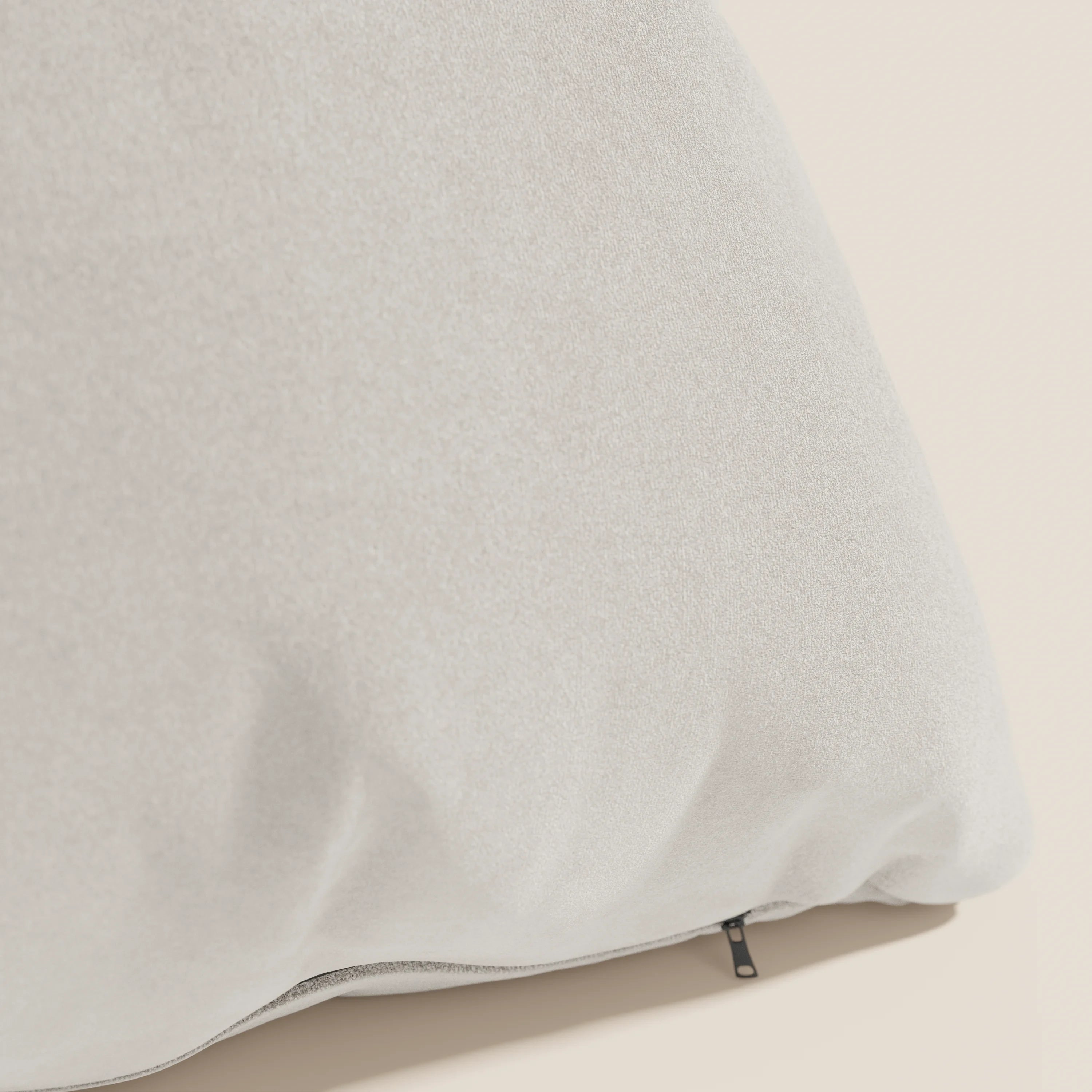 Un primo piano del cuscino Jazz di Divani.Store, in smacchiabile microfibra panna T11, mostra la sua morbida consistenza e la discreta cerniera nera lungo il bordo inferiore, su uno sfondo beige chiaro.