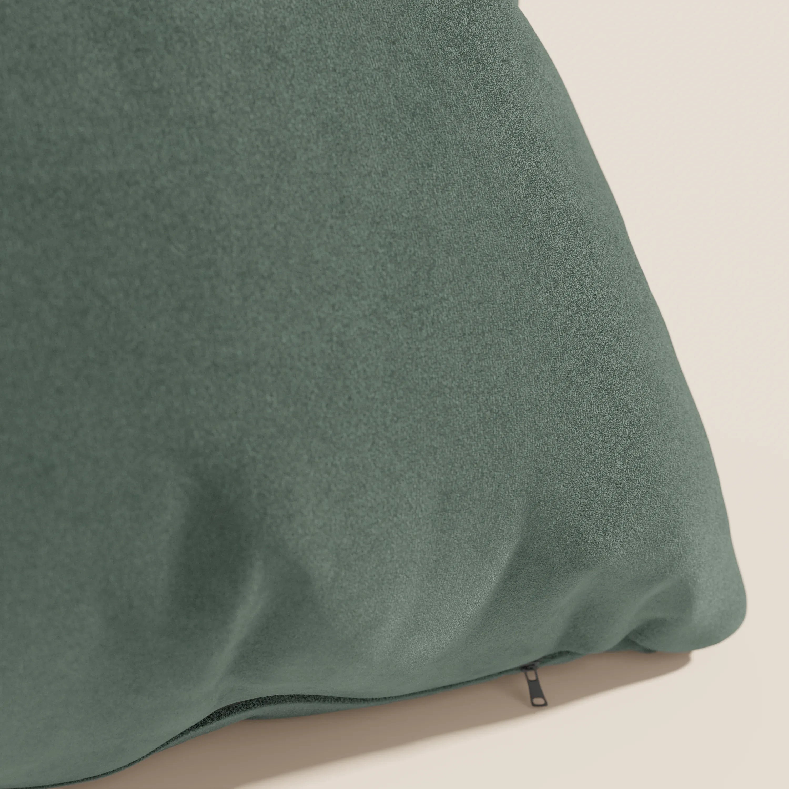 Primo piano del cuscino Jazz 45x45 di Divani.Store in T11 verde, realizzato in microfibra tecnica antimacchia. Il cuscino verde scuro è morbido al tatto, con pieghe sottili e una cerniera nera sul bordo inferiore su uno sfondo beige chiaro.