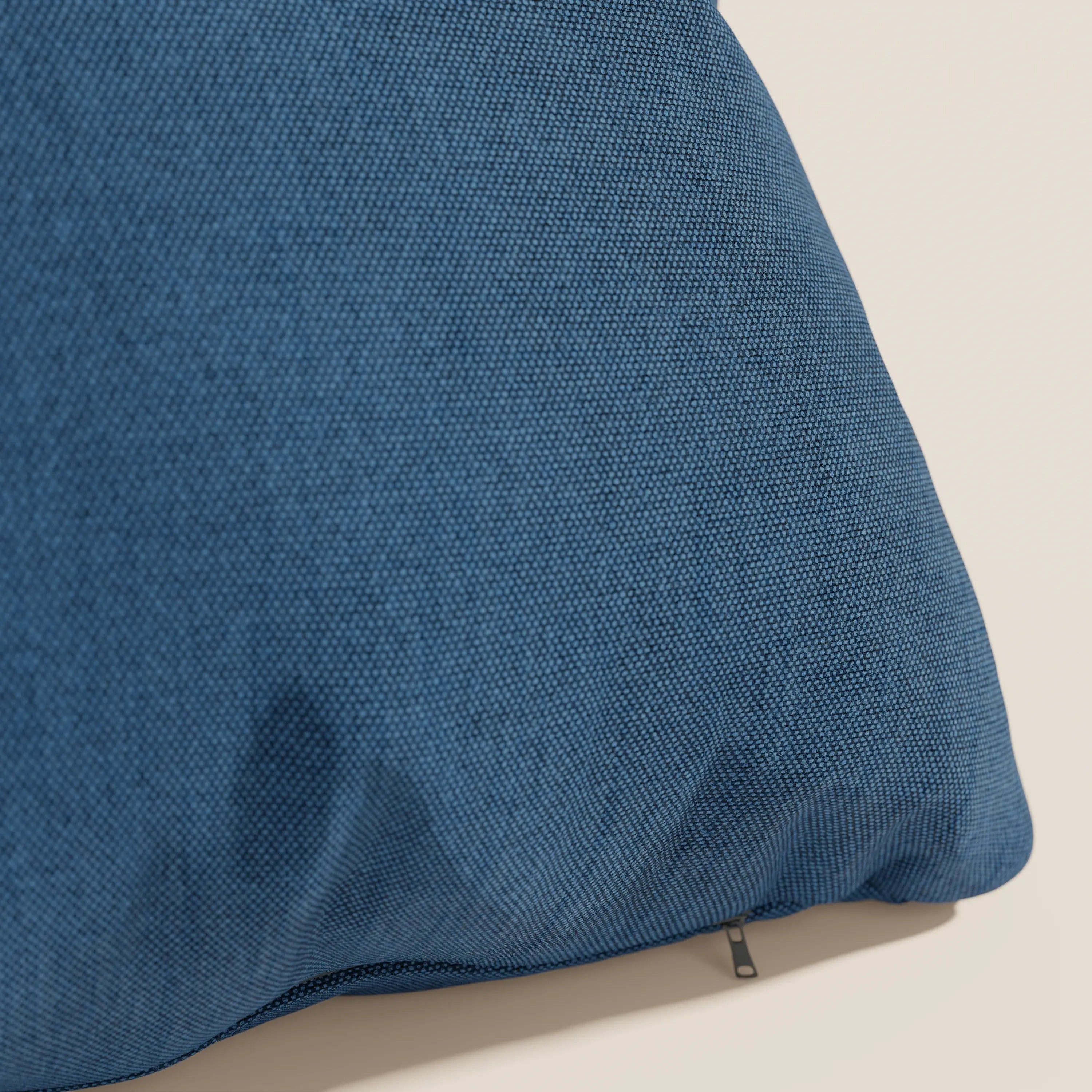 Un primo piano del cuscino Honey 45x45 di Divani.Store in tessuto simil cotone impermeabile T13 blu mostra la cerniera a vista e il bordo curvo su uno sfondo beige chiaro che ne evidenzia la qualità e il design.