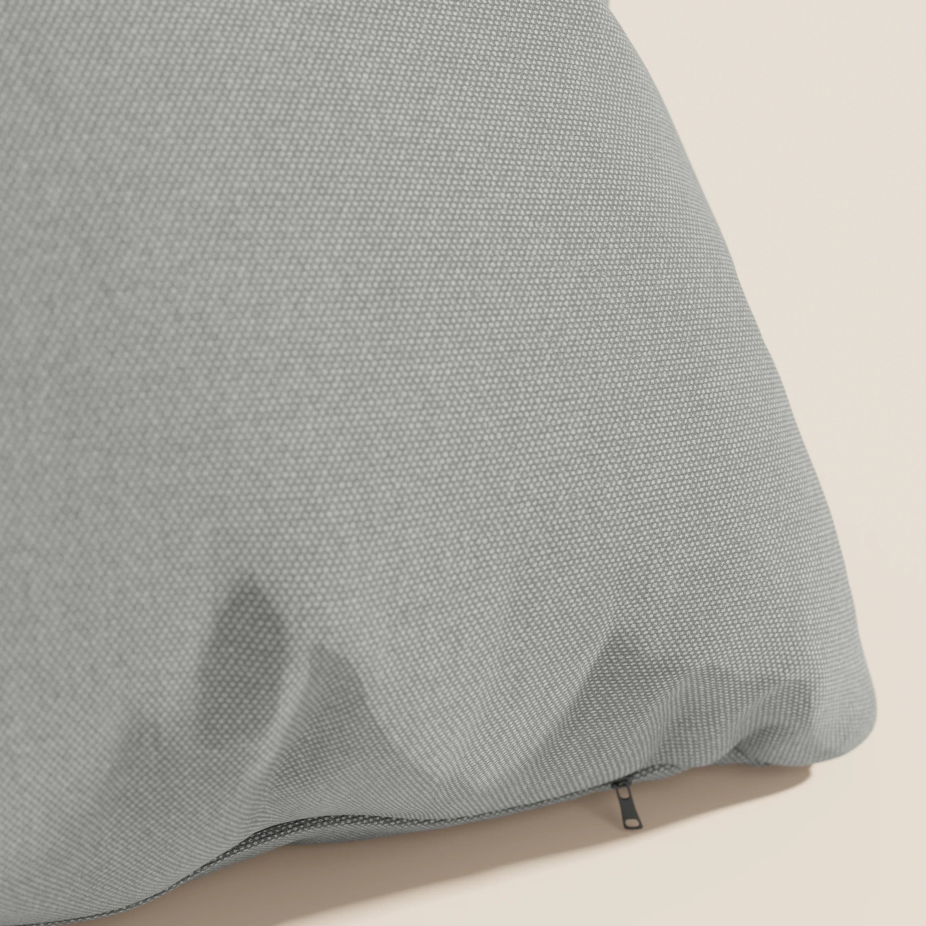 Primo piano del cuscino Honey 45x45 cm di Divani.Store in impermeabile T13 grigio simil cotone, caratterizzato da una superficie morbida e da una cerniera nera parzialmente visibile lungo un bordo, su sfondo beige.