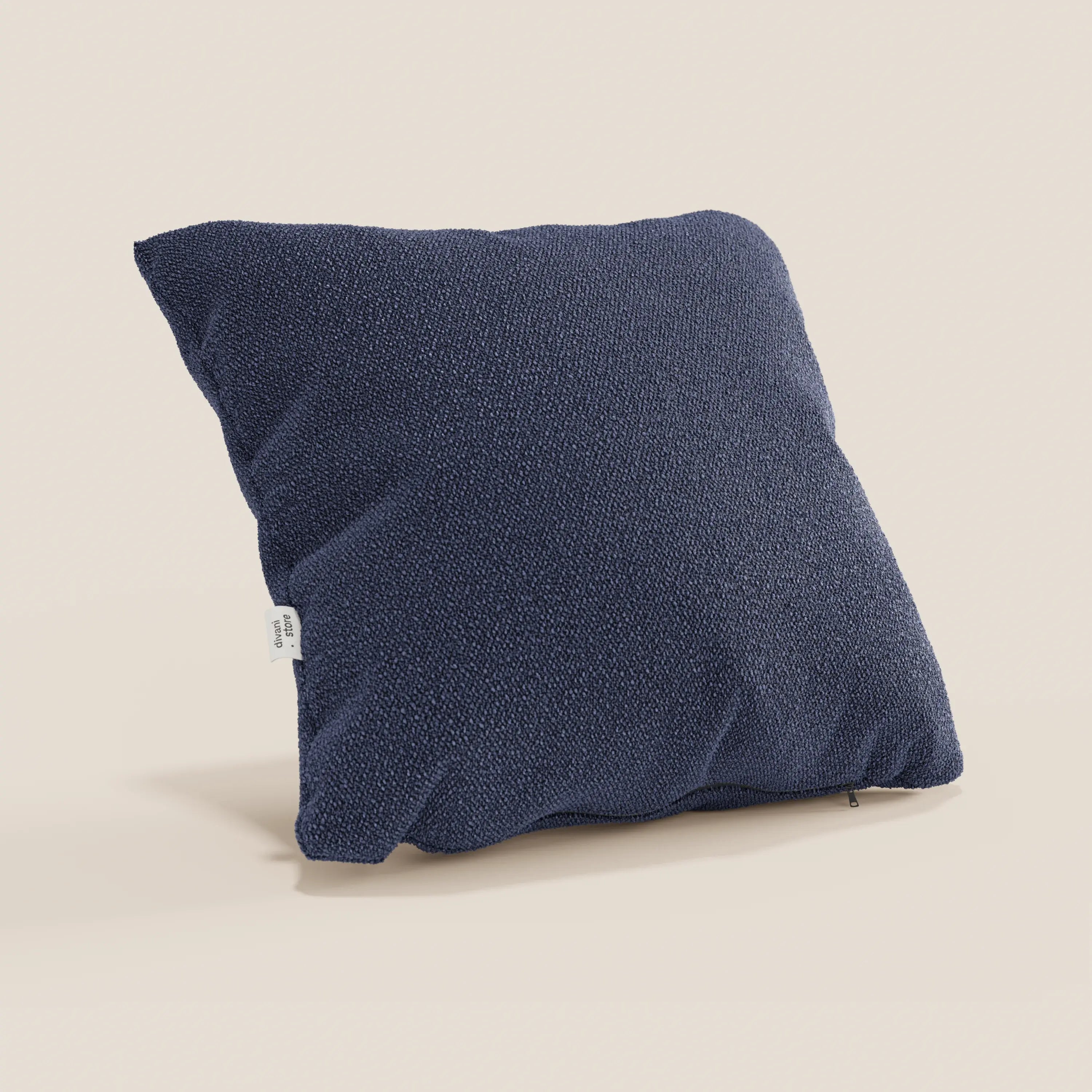 Il cuscino Lambada di Divani.Store, di forma quadrata e di colore blu navy, si trova su uno sfondo beige chiaro. Realizzato in fresco tessuto T33 antimacchia e impermeabile, dall'aspetto naturale, è caratterizzato da un design minimalista con una piccola etichetta bianca sul lato.