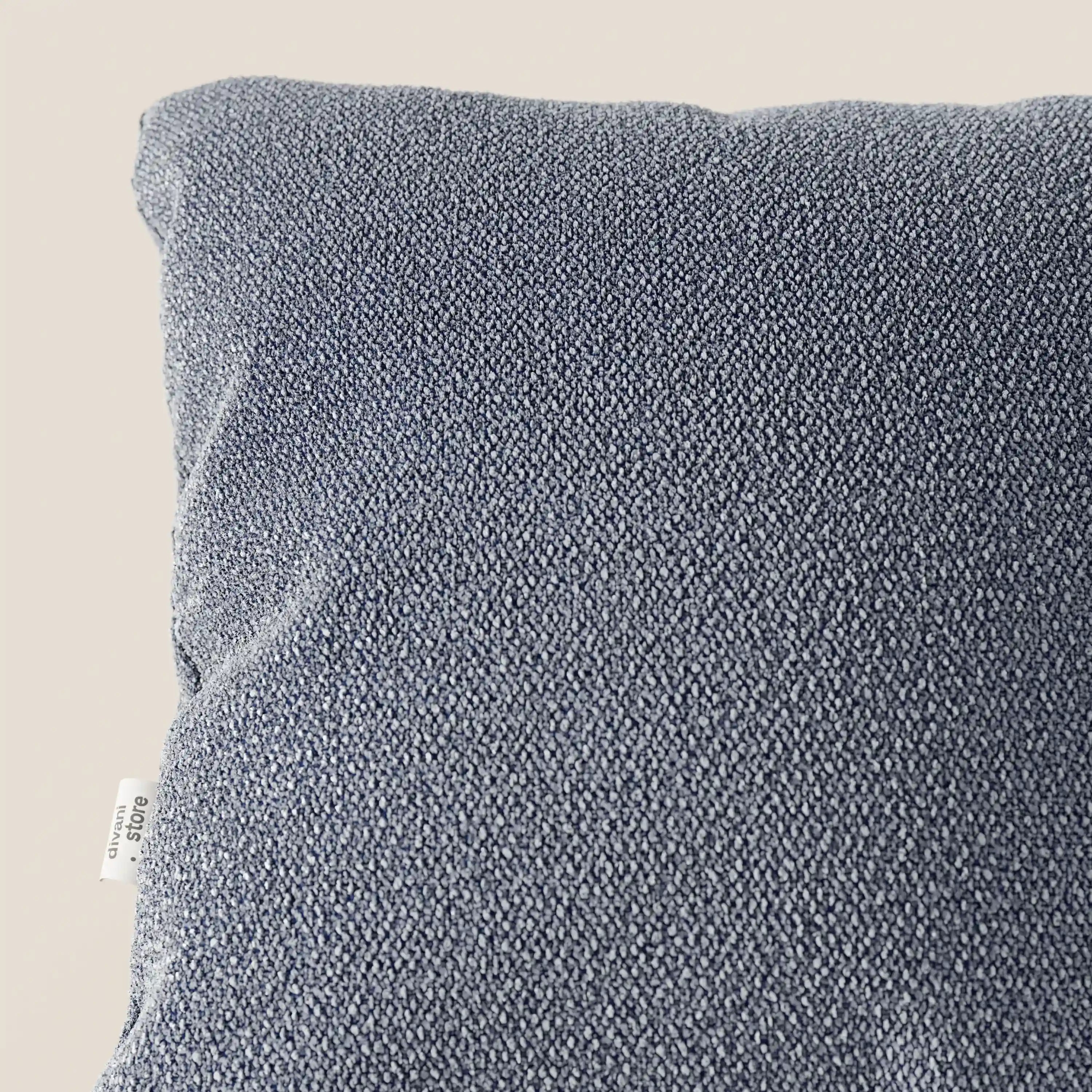 Primo piano del cuscino Lambada di Divani.Store, in tessuto grigio-azzurro che sembra cotone naturale. Resistente alle macchie e all'acqua (T33), presenta una finitura intrecciata con una piccola etichetta bianca sul bordo sinistro.