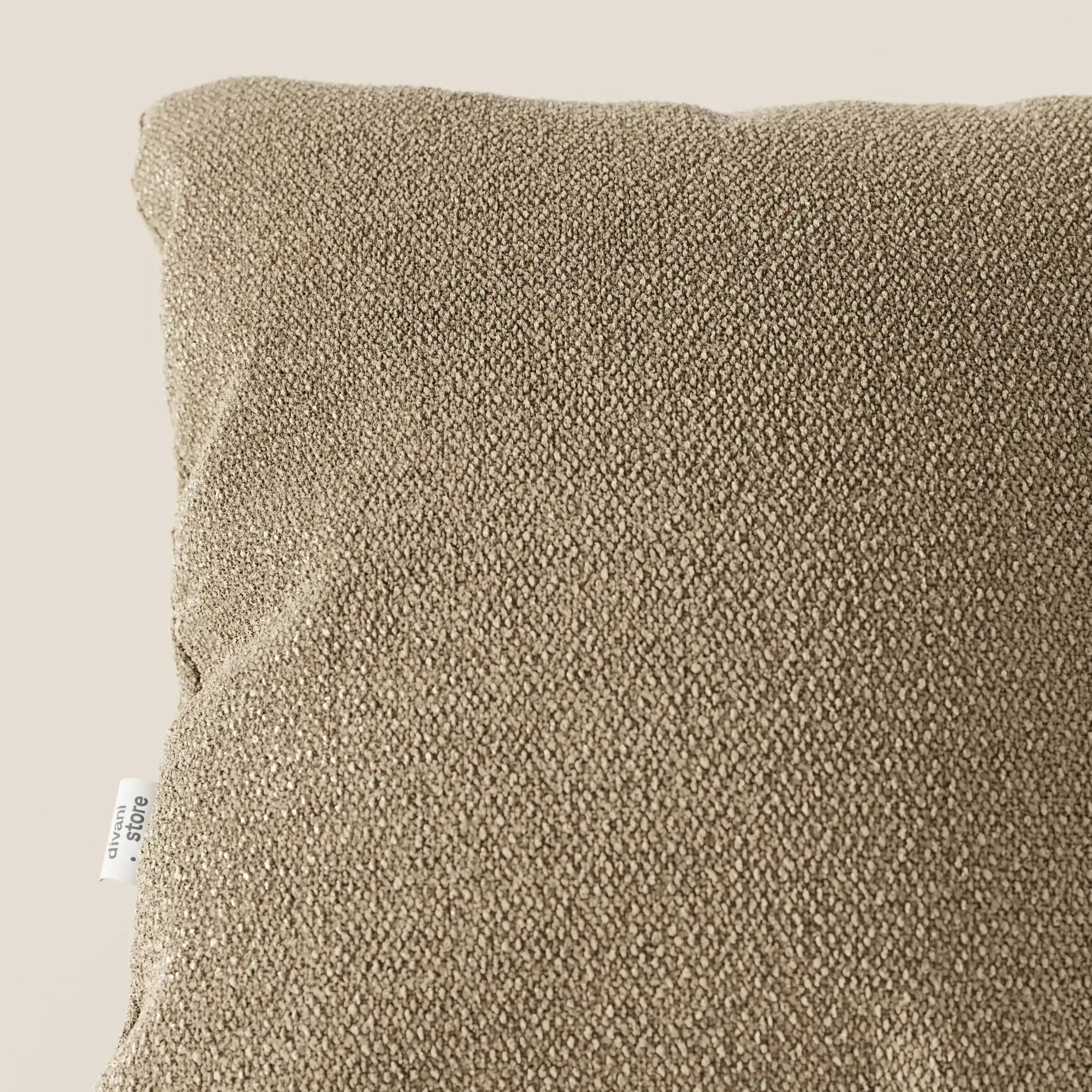 Primo piano dell'angolo superiore sinistro di un cuscino Lambada di Divani.Store in color tortora, realizzato in tessuto naturale tipo cotone T33, fresco, antimacchia e impermeabile. Una piccola etichetta bianca con testo è visibile sulla cucitura sinistra; la superficie appare morbida e leggermente irregolare.