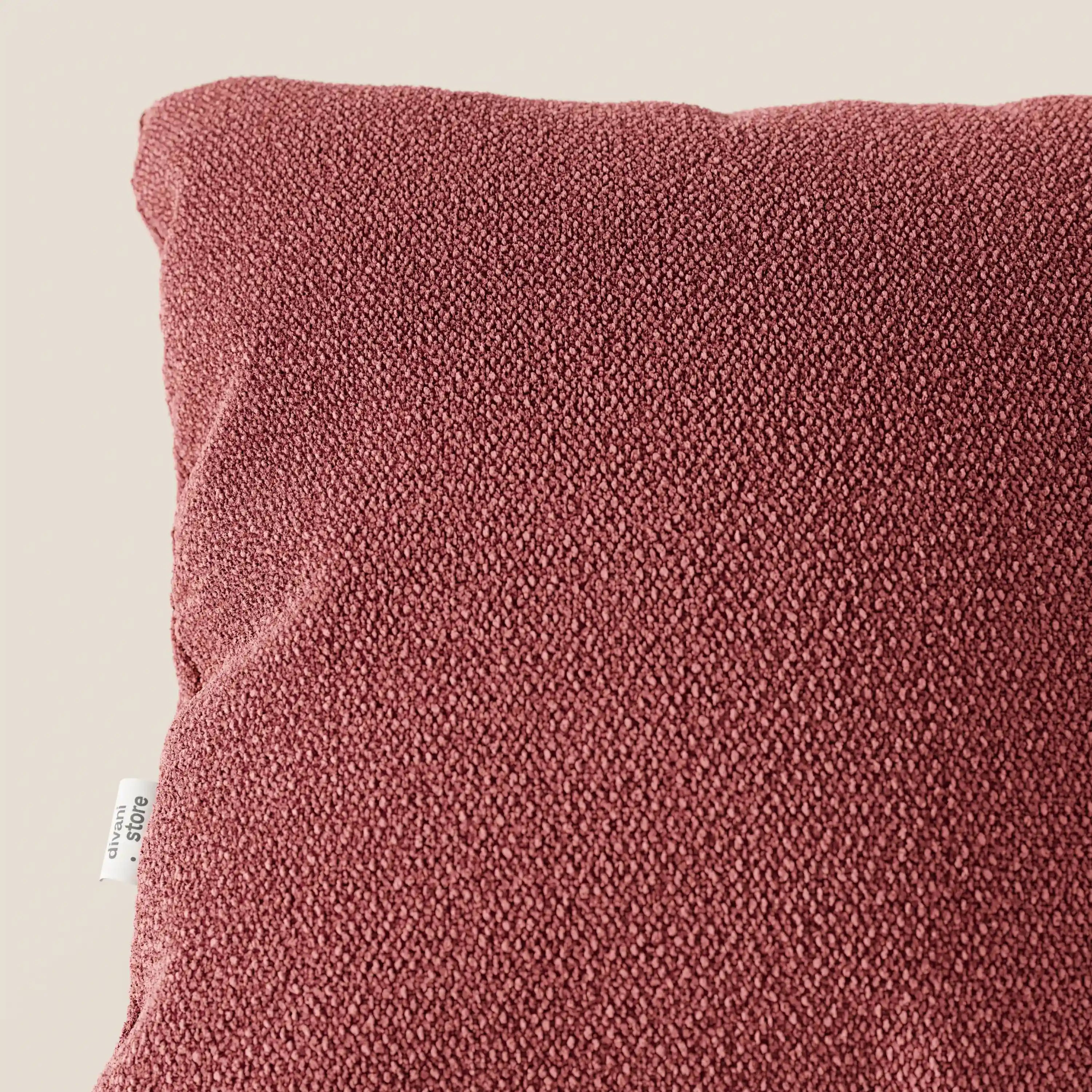 Primo piano del cuscino Lambada di Divani.Store, in tessuto T33 rosso scuro, testurizzato, simile al cotone, smacchiabile e impermeabile, su sfondo beige. Una targhetta bianca con testo appare sul bordo sinistro del cuscino.