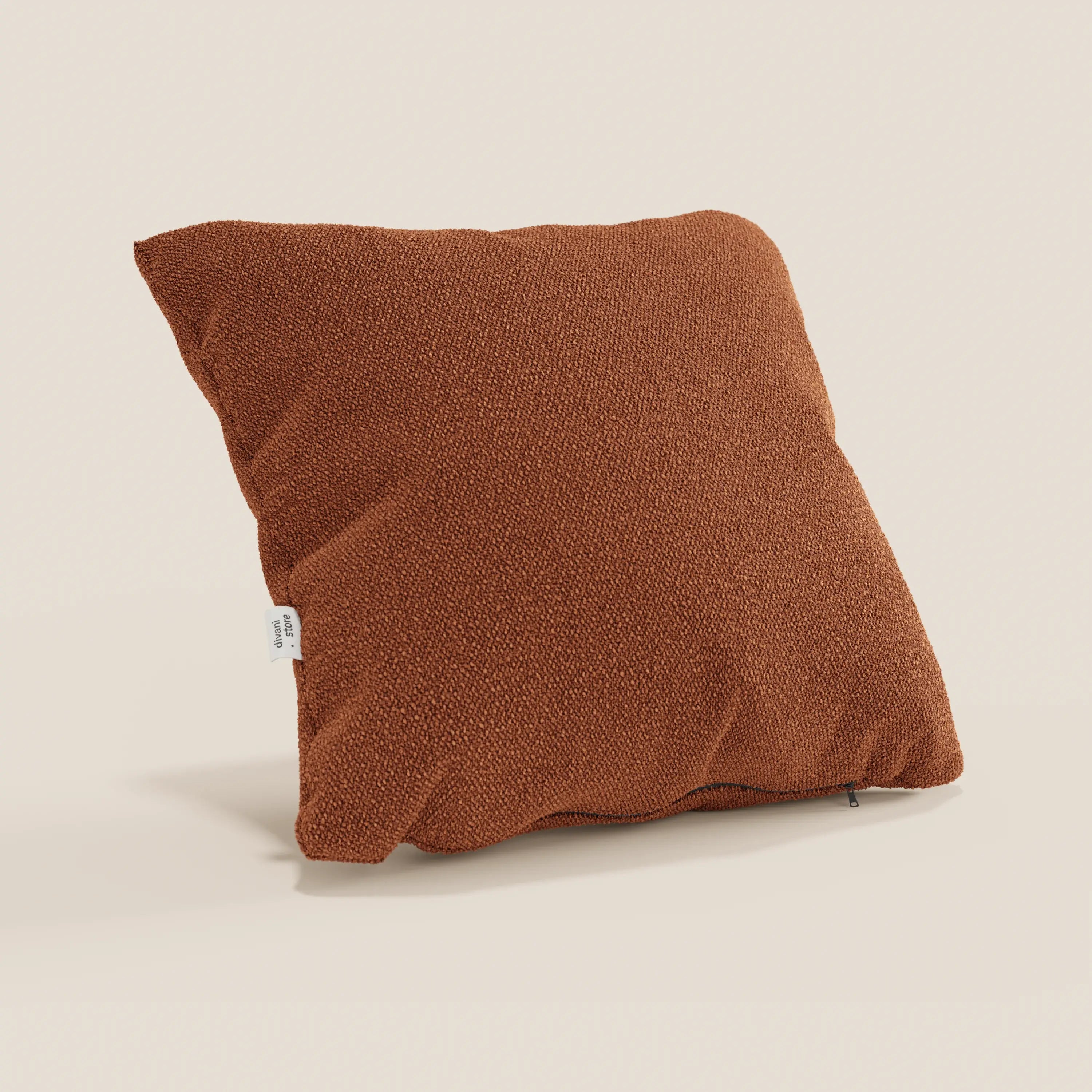 Divani.Store presenta un cuscino Lambada quadrato color ruggine su uno sfondo beige chiaro. Realizzato in tessuto naturale simil-cotone (T33), fresco, lavabile e impermeabile, presenta una superficie strutturata e una piccola etichetta laterale bianca.