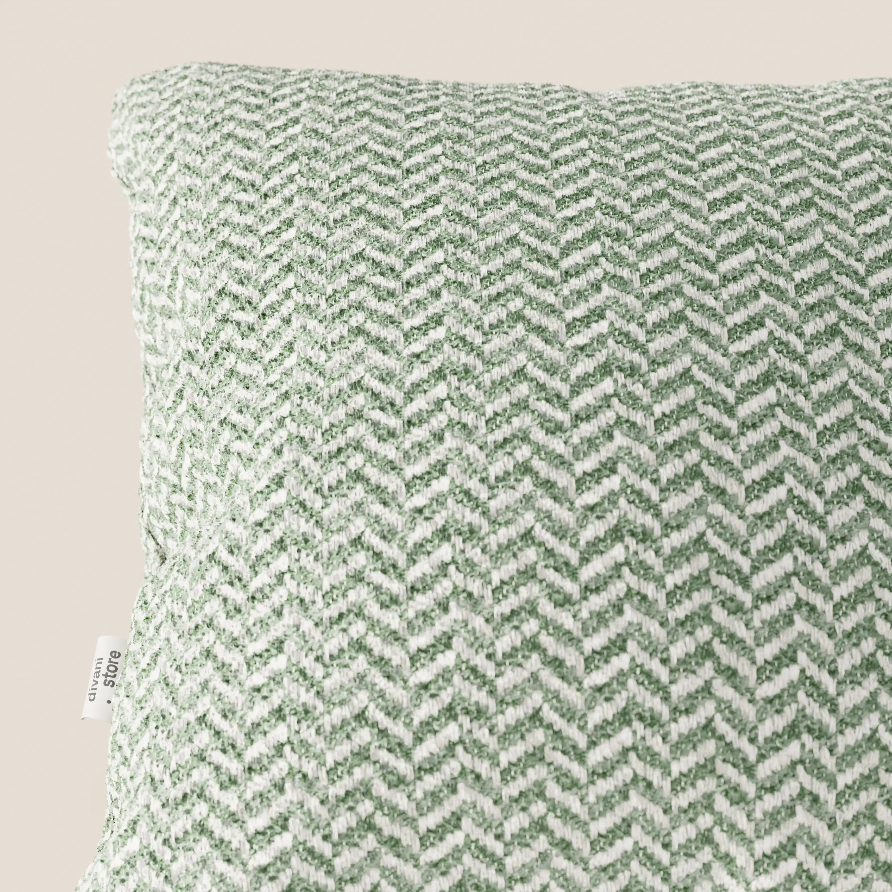Un primo piano del cuscino Sorrento 45x45 in Lino di Divani.Store ne mette in risalto il motivo a chevron intrecciato verde e bianco, il tessuto testurizzato e l'etichetta in tessuto sul bordo sinistro. Lo sfondo beige chiaro esalta questo elegante cuscino lavabile in lavatrice.