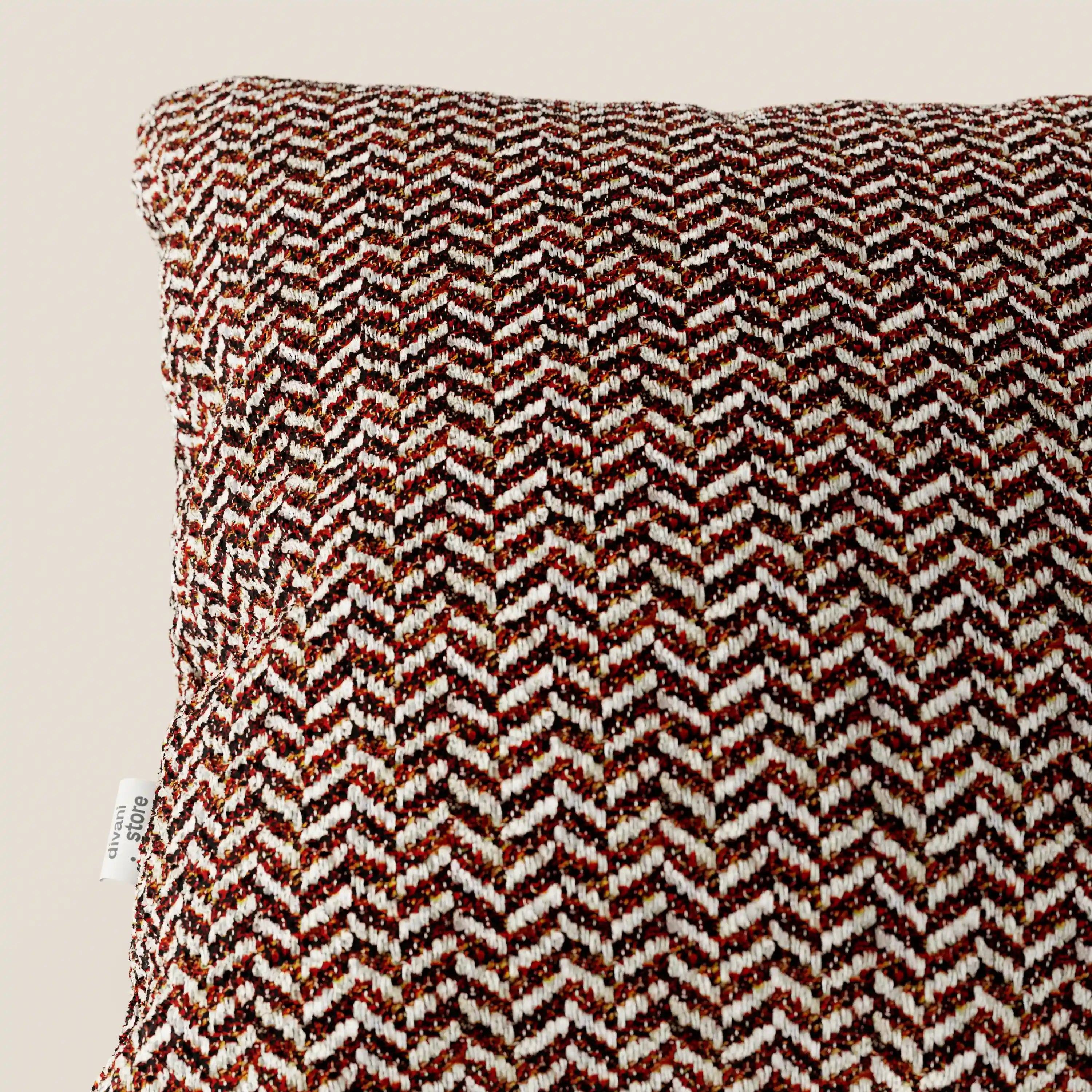 Primo piano del cuscino Sorrento 45x45 in lino di Divani.Store, caratterizzato da un motivo a chevron nei toni del marrone, ruggine e crema, con un'etichetta in tessuto bianca. Questo cuscino lavabile in lavatrice unisce praticità ed eleganza naturale su uno sfondo beige.