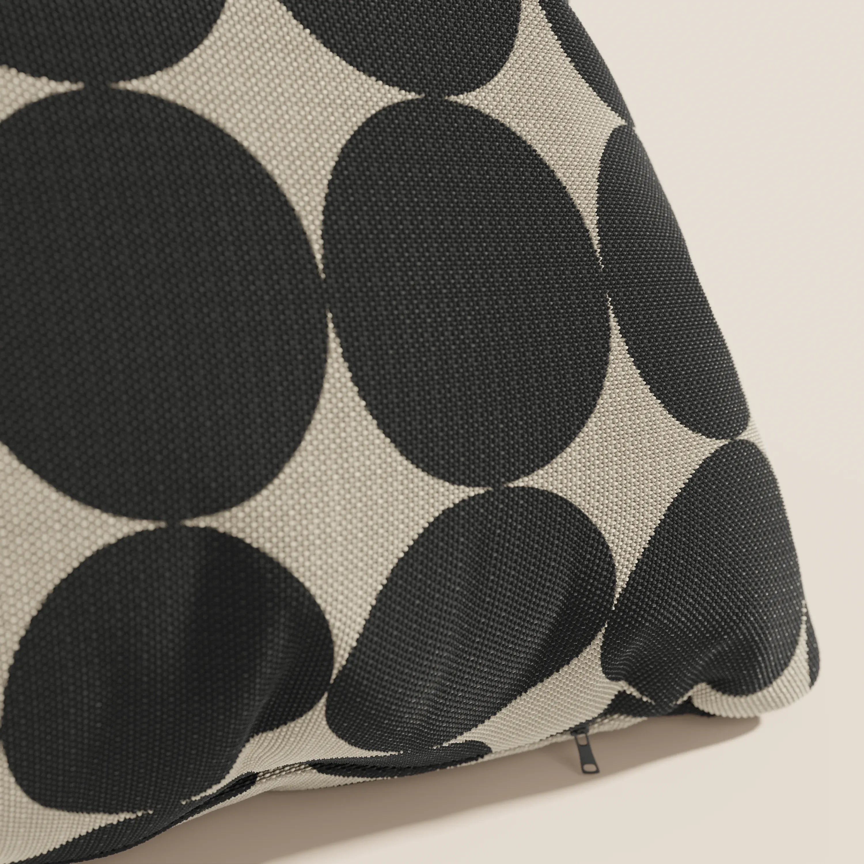 Primo piano dei cuscini geometrici Dot di Divani.Store in tessuto tortora idrorepellente, caratterizzati da un'audace fantasia a cerchi geometrici neri e beige e da una piccola cerniera nera vicino al bordo.