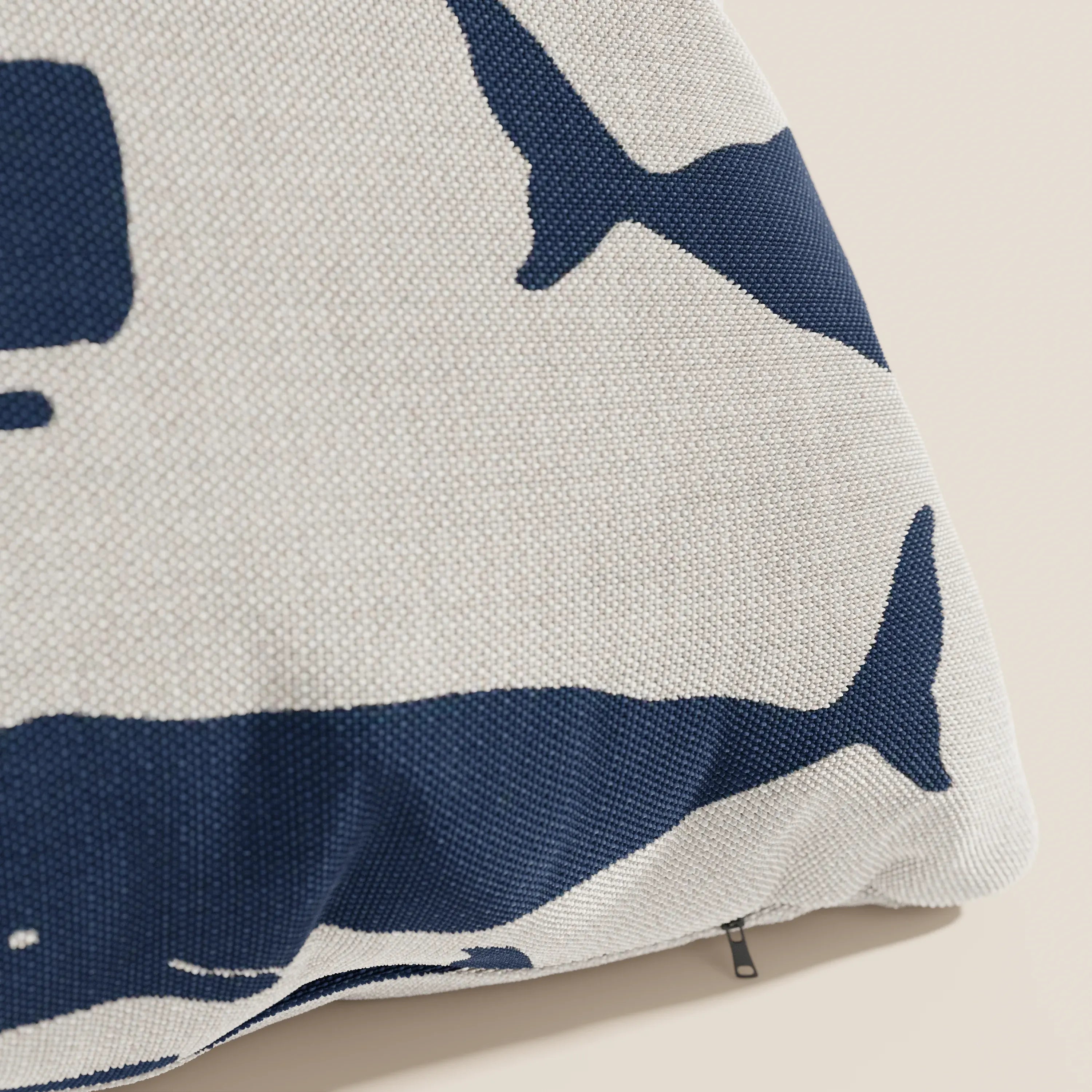 Primo piano della collezione di cuscini Divani.Store Nautilus in tessuto impermeabile balena, con grandi sagome di balene blu scuro su una superficie imbottita bianco sporco e una piccola cerniera sul fondo.