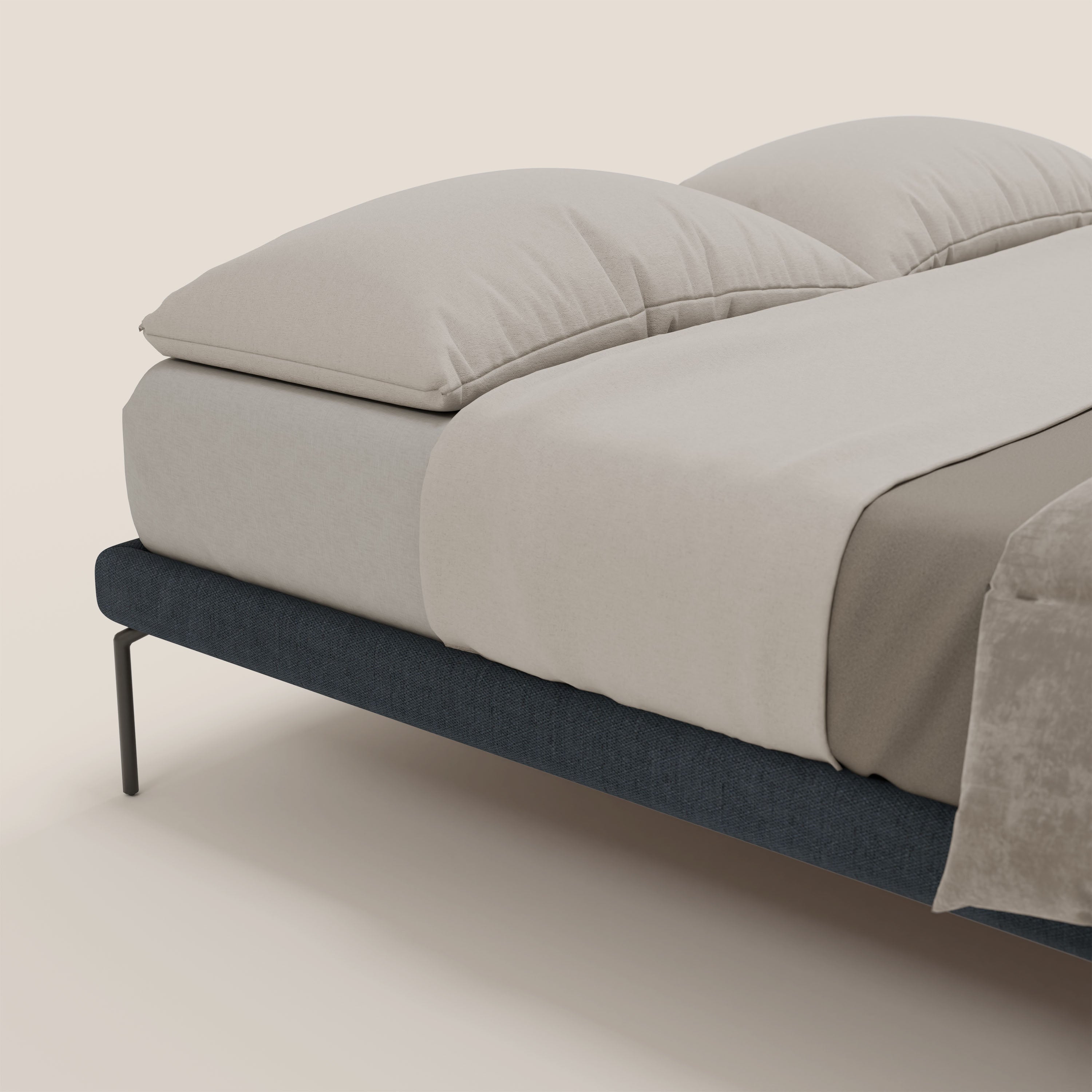 Il sommier sfoderabile Letti.store Ring è caratterizzato da alte gambe nere da 24 cm e da un tessuto impermeabile blu T14, qui proposto con lenzuola e cuscini beige chiaro per un look minimalista e accogliente su uno sfondo neutro.