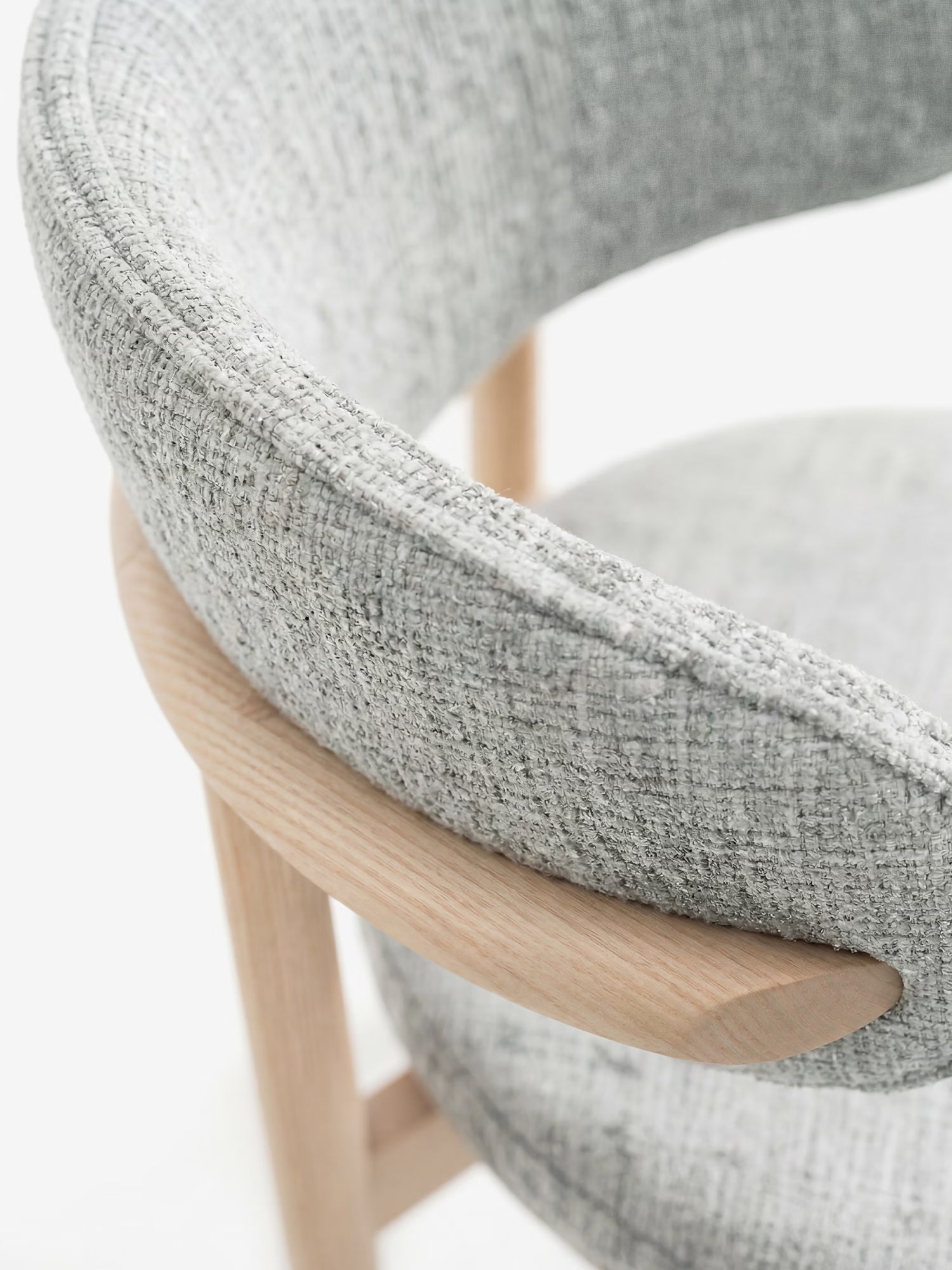 Primo piano della sedia imbottita Dafne di Divani.Store, realizzata con tessuto chenille certificato OEKO-TEX® in grigio chiaro su seduta e schienale curvi, con gambe in rovere massello naturale, che mette in risalto il suo design minimalista e contemporaneo su uno sfondo bianco.