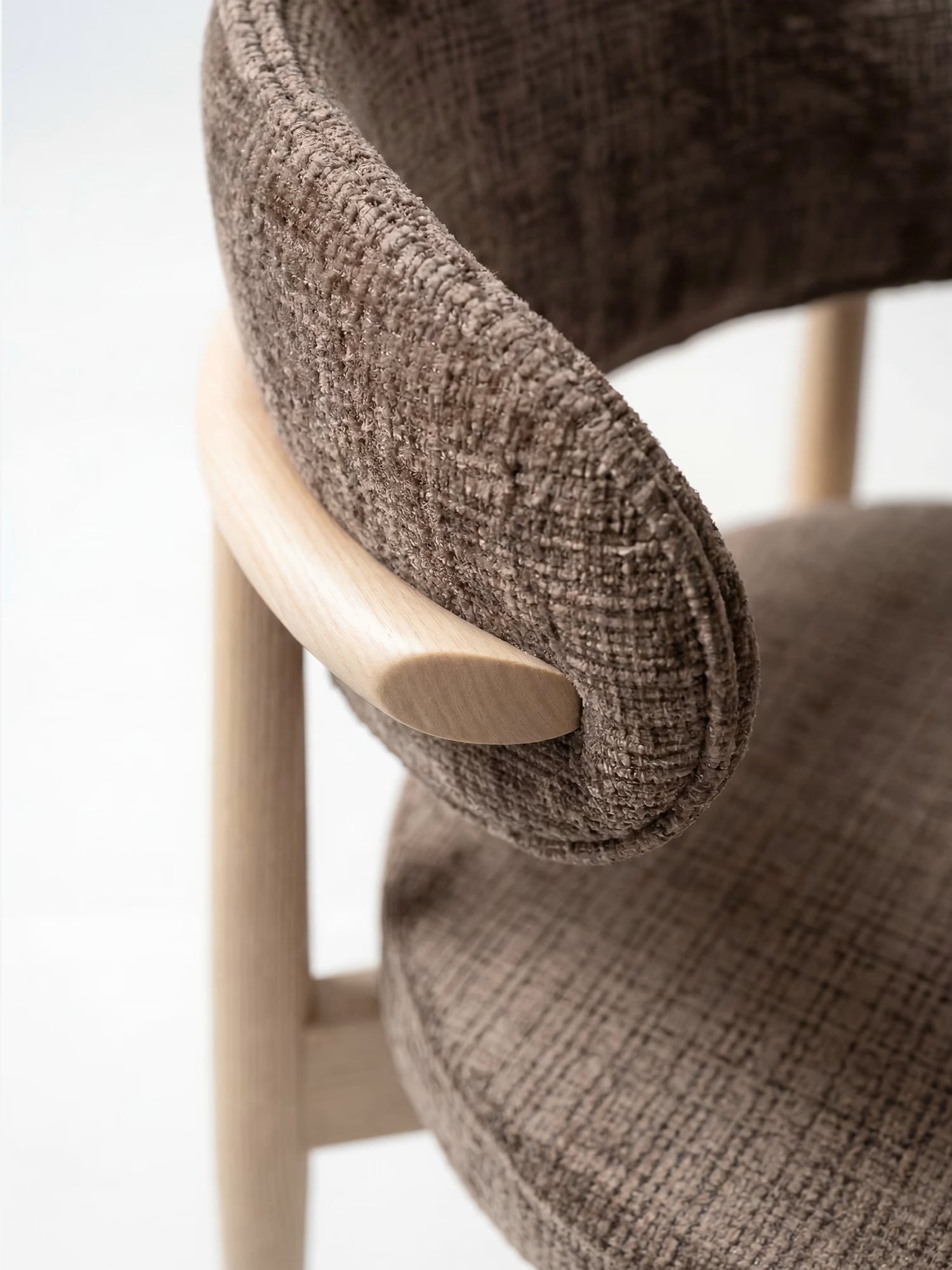 Primo piano della sedia imbottita Dafne di Divani.Store, caratterizzata da uno schienale curvo in tessuto ciniglia certificato OEKO-TEX® e da una struttura in rovere massello naturale, che ne esalta il design minimalista su uno sfondo neutro.
