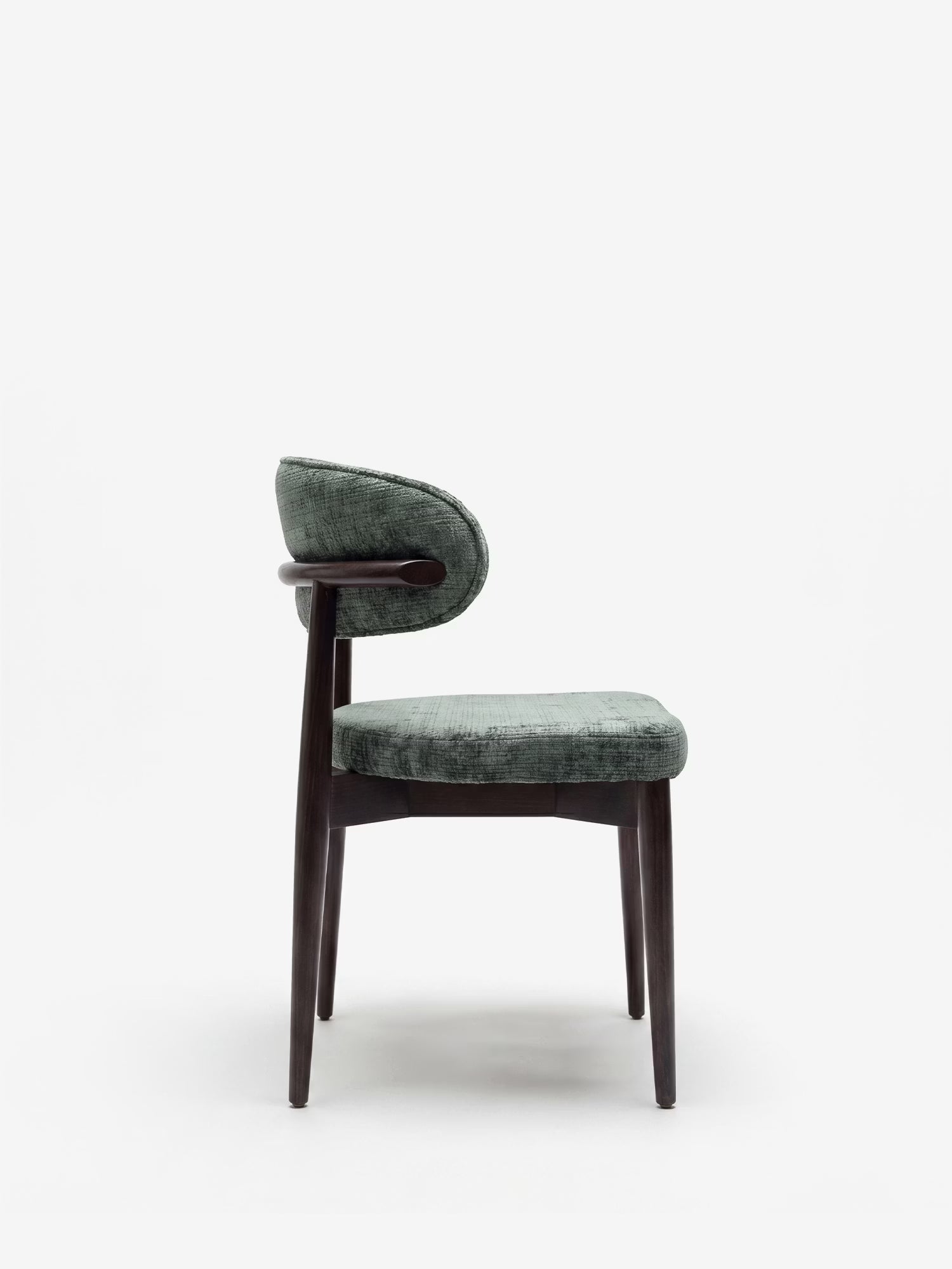Vista laterale della sedia imbottita Dafne di Divani.Store, caratterizzata da uno schienale imbottito curvo e da una seduta imbottita in ciniglia verde tenue certificata OEKO-TEX®, con struttura e gambe in legno massello di wengé, su uno sfondo bianco a tinta unita.