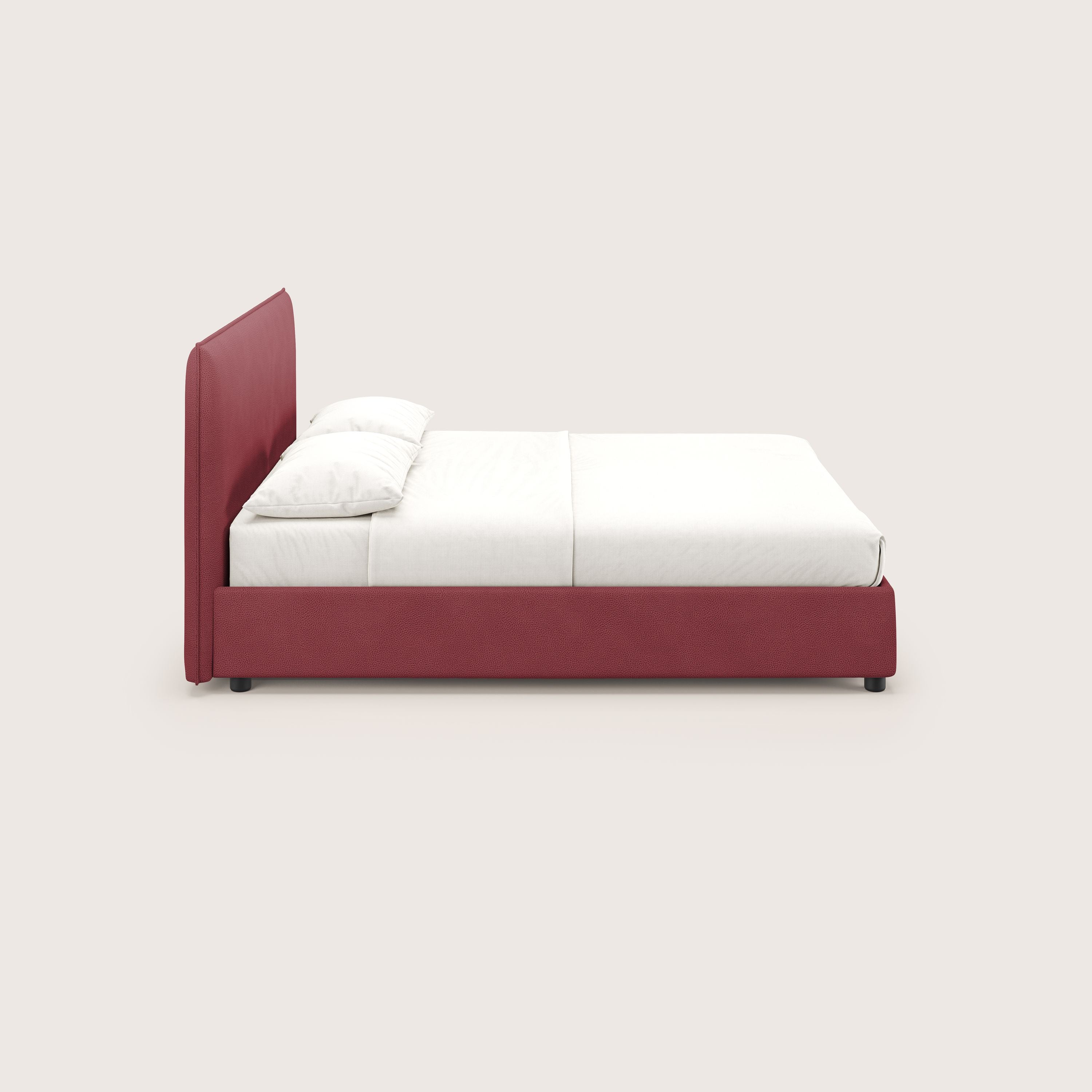 Una vista laterale del letto Nina contenitore dal design minimal in microfibra effetto pelle smacchiabile rosso di Letti.store, caratterizzato da un'alta testata e una base imbottite rosse, con biancheria da letto bianca, evidenzia il minimalismo italiano su uno sfondo bianco sporco.