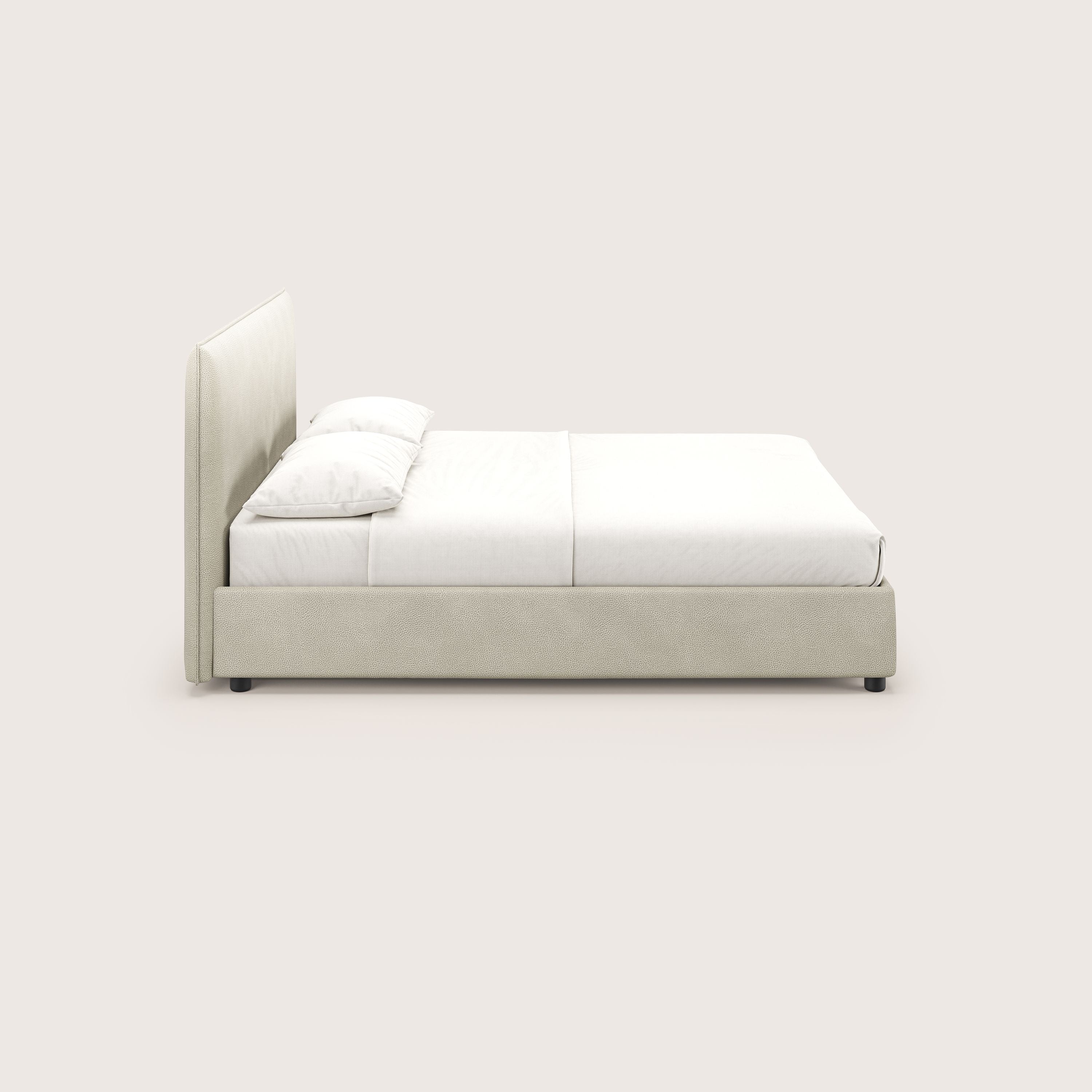Vista laterale di Nina letto contenitore di Letti.store - design minimal in microfibra effetto panna antimacchia, con testiera e struttura imbottite, lenzuola e cuscini bianchi. Il morbido sfondo bianco sporco evidenzia il suo moderno stile italiano.