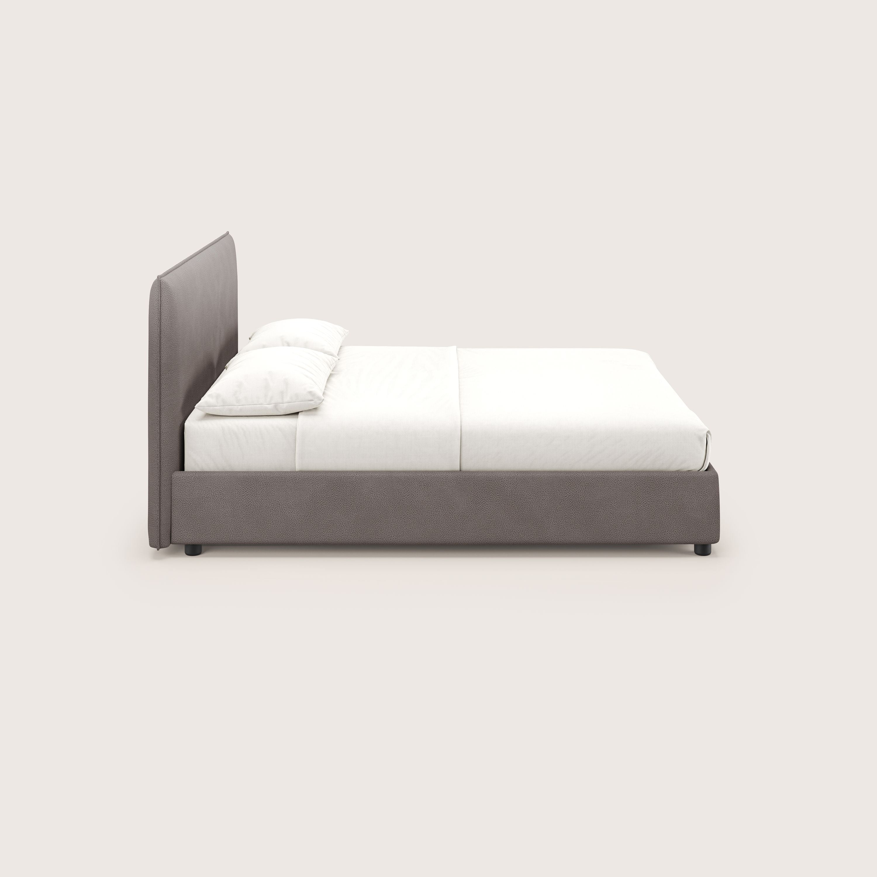 Una vista laterale del letto contenitore Nina di Letti.store mostra un design minimale in microfibra marrone antimacchia effetto pelle, con un'alta testata imbottita, biancheria da letto bianca, due cuscini e un materasso basso e spesso.