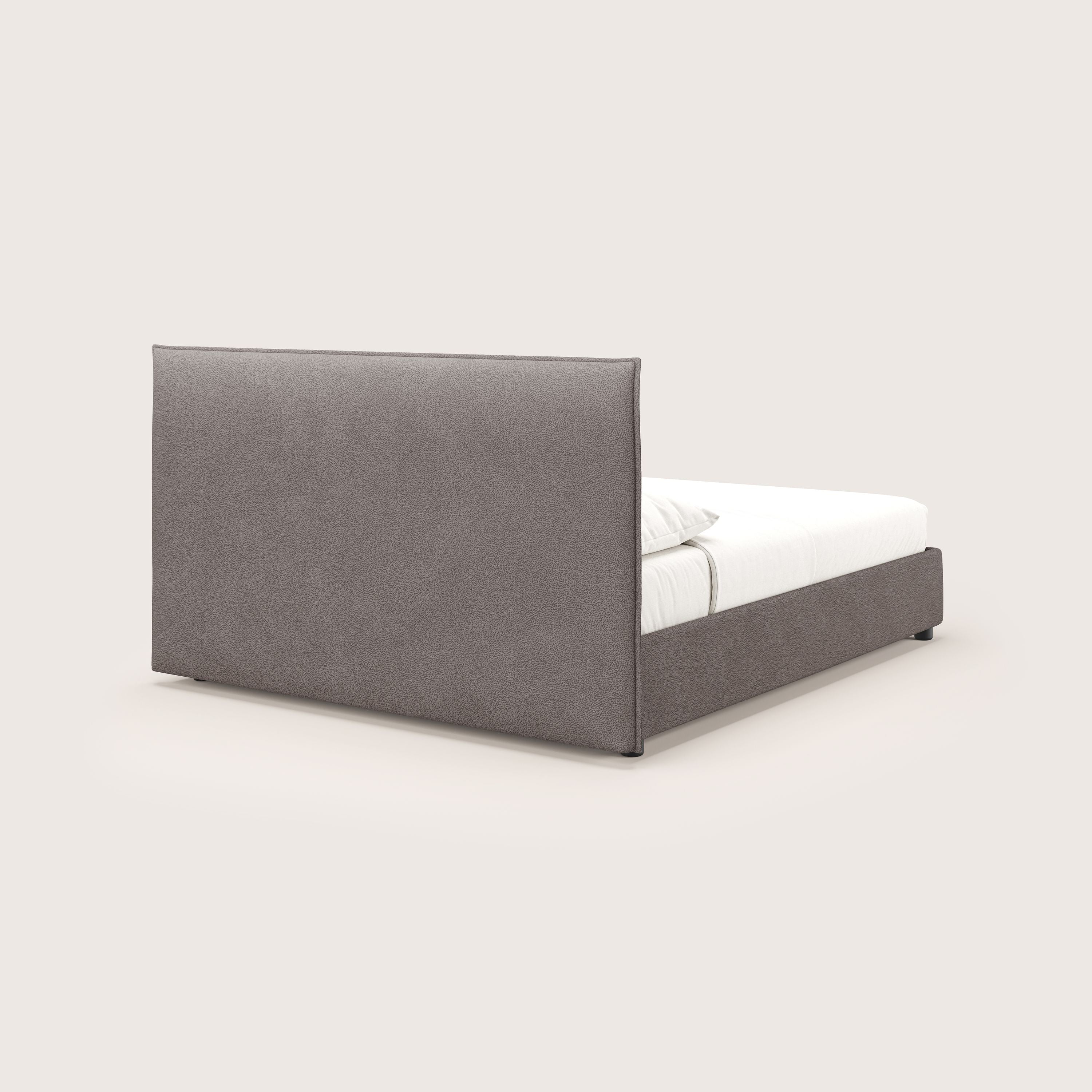 Il letto contenitore Nina di Letti.store è caratterizzato da un design minimale in microfibra marrone antimacchia effetto pelle, con un'alta testata imbottita e una base coordinata, presentata con un materasso bianco e due cuscini su uno sfondo bianco sporco.